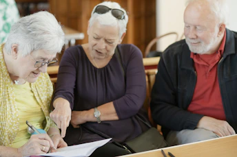 Three older adults are looking at a paper.