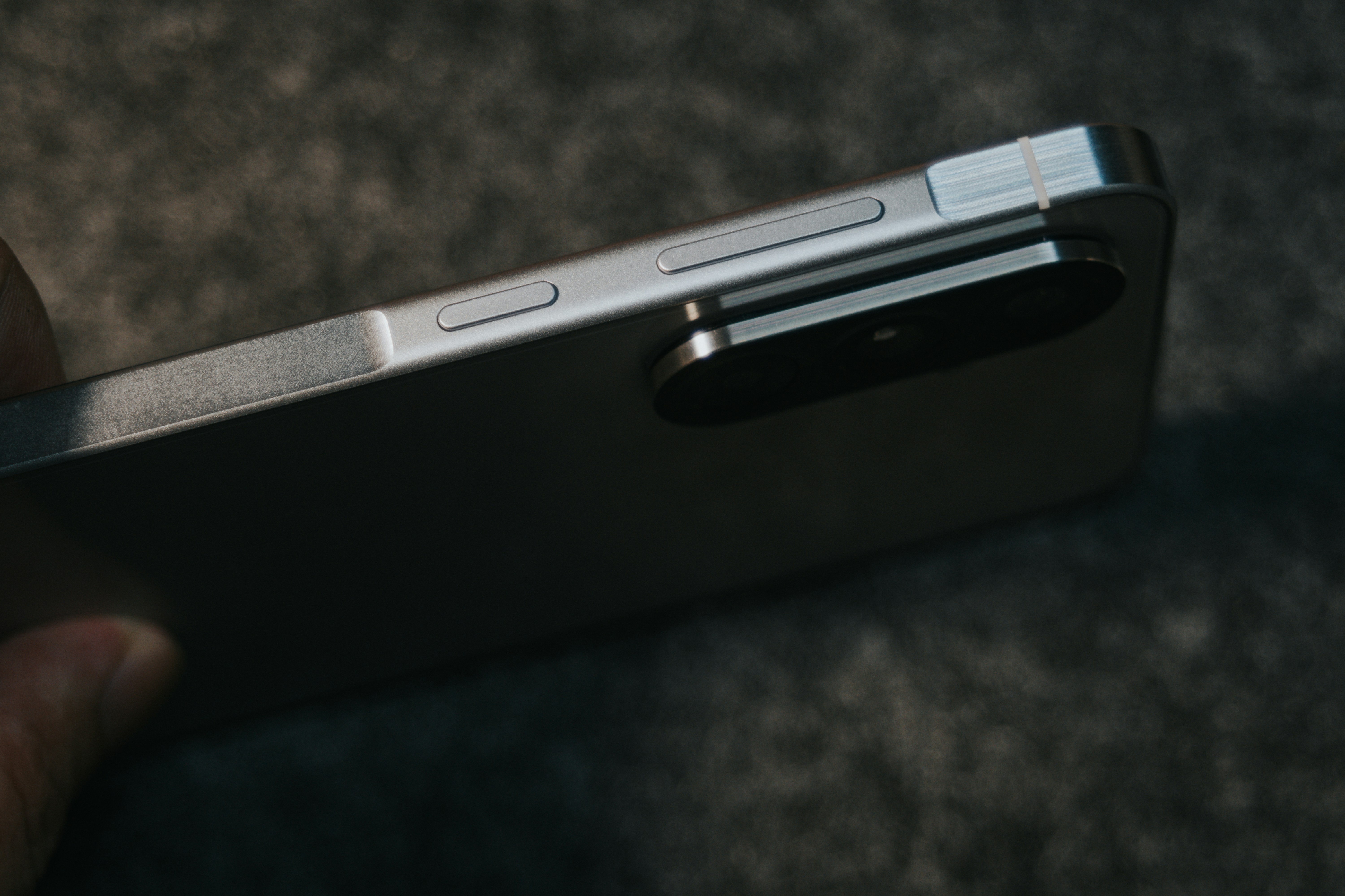 Person holding sleek titanium Android smartphone outdoors camera bar detail