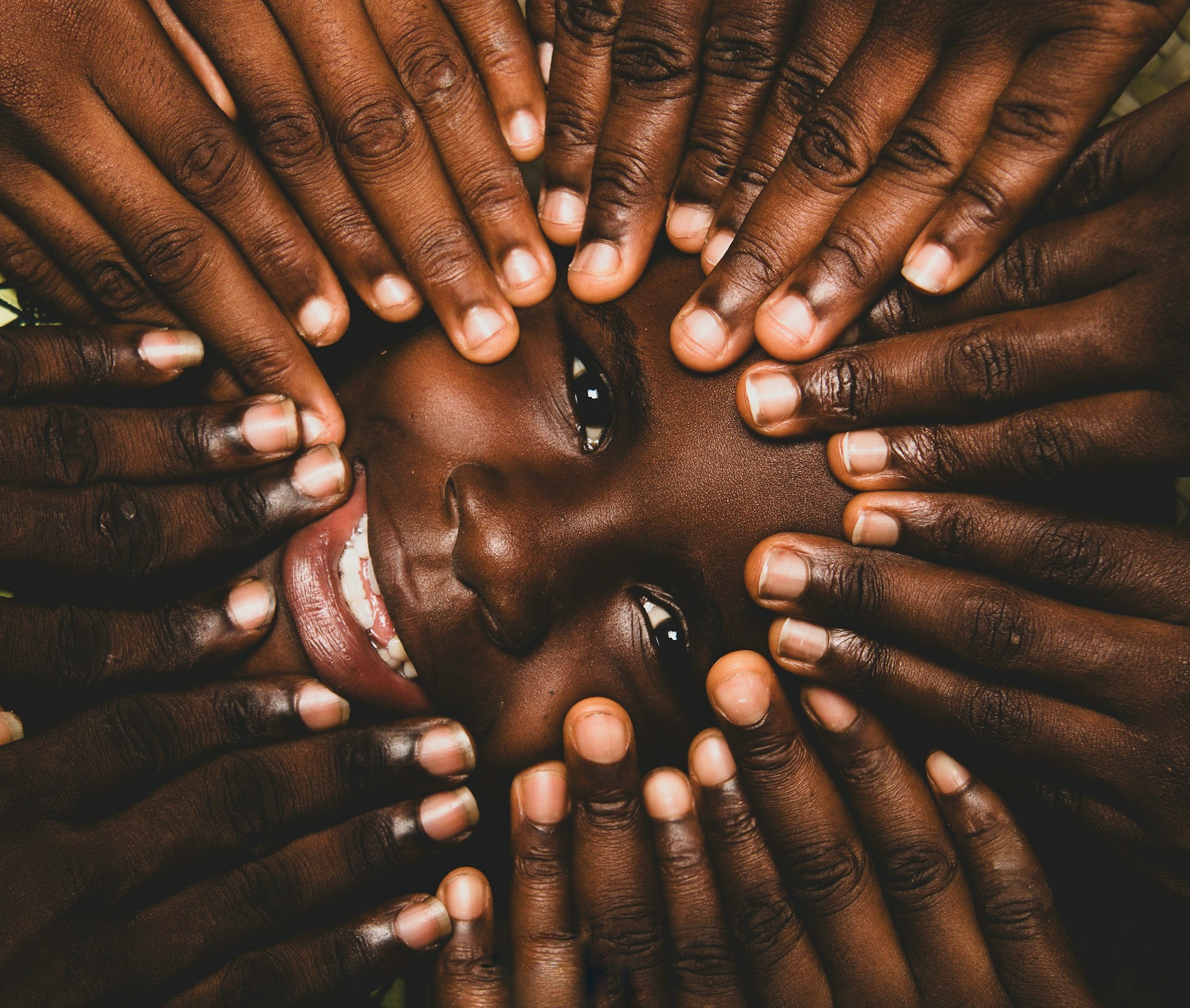 A child surrounded by hands, peeking through.