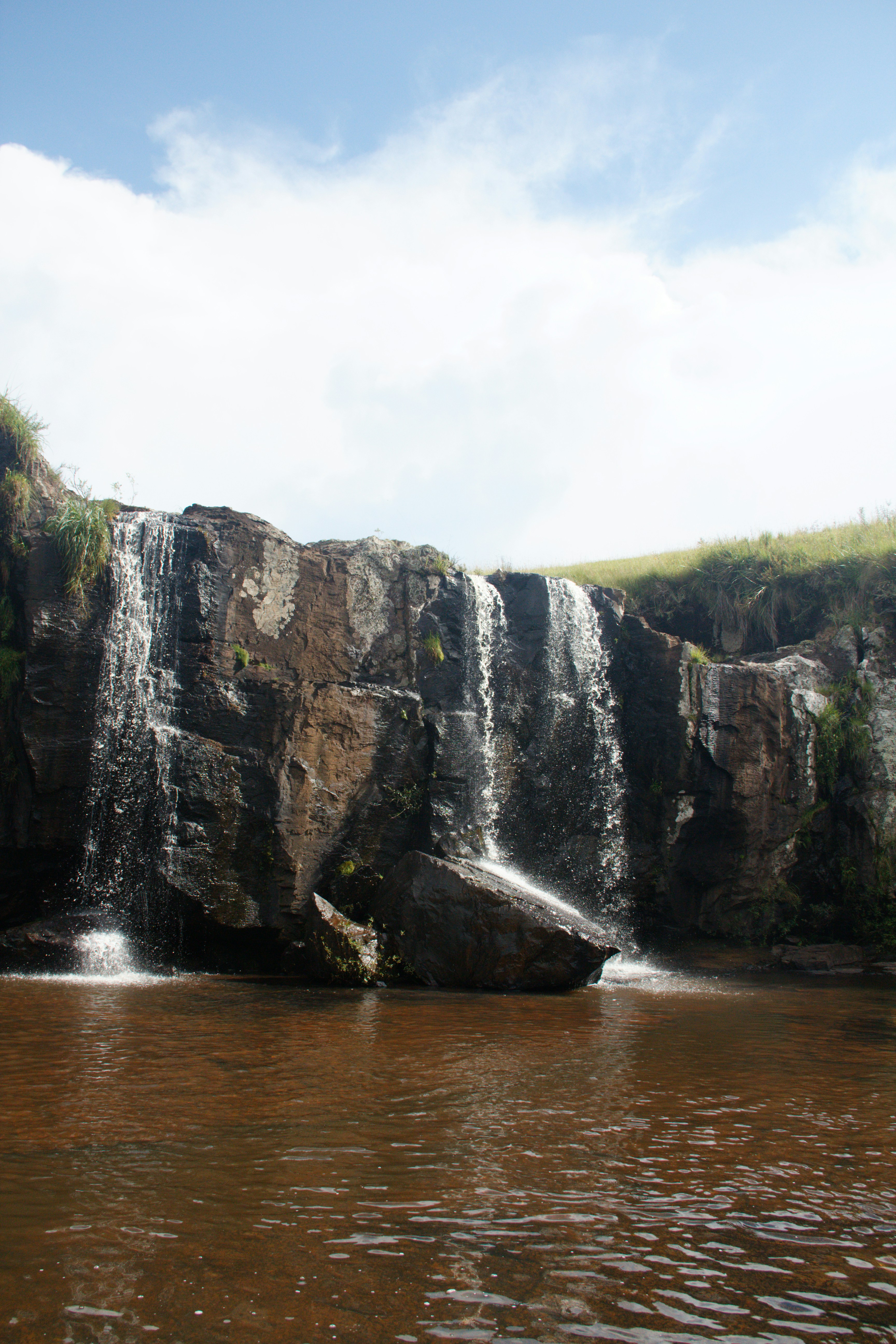 A waterfall cascades into a dark, muddy pool.
