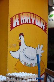 A cheerful chicken advertises eggs on a yellow wall.