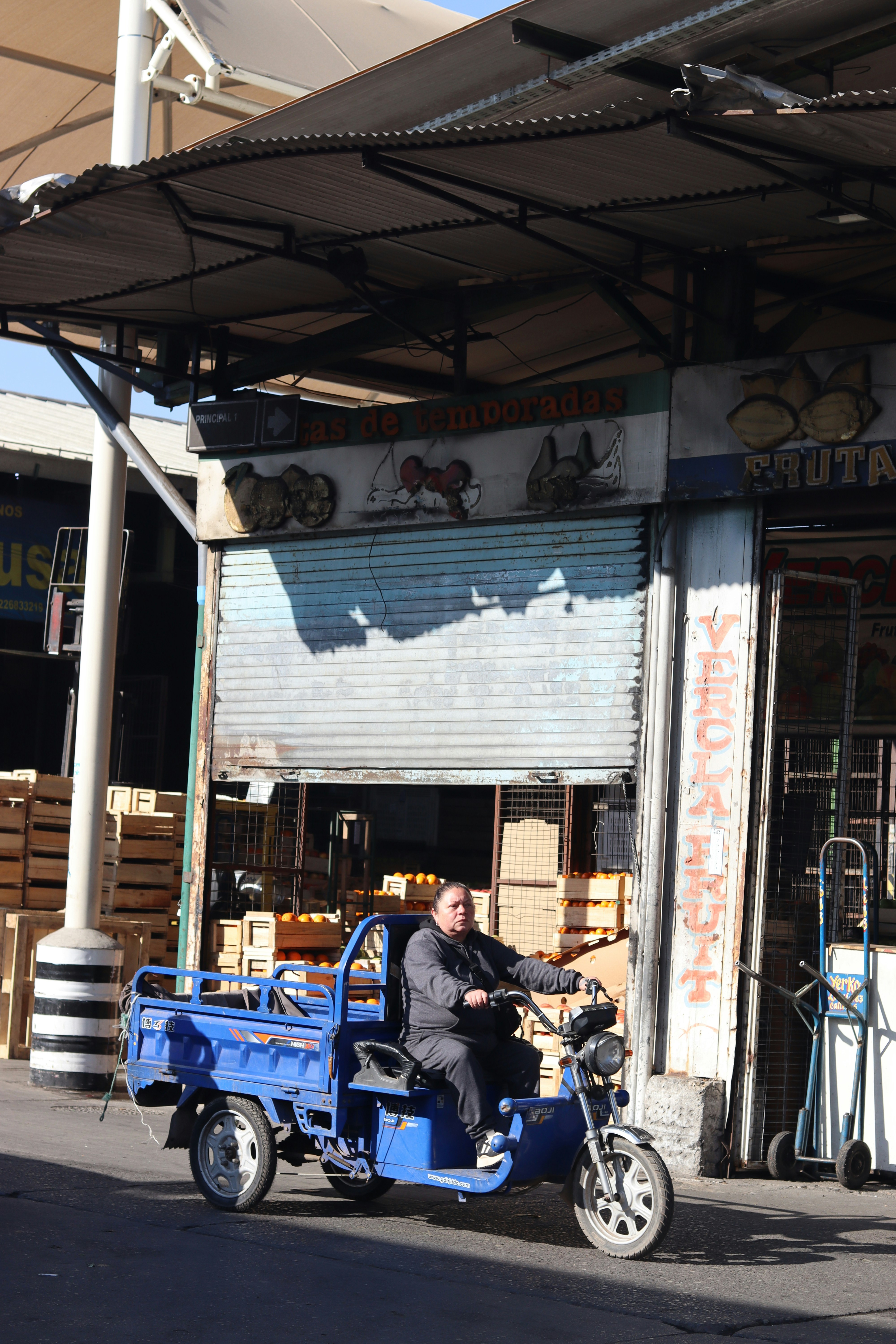 Una persona conduce un triciclo frente a un mercado.
