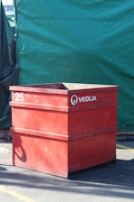 Red veolia bin sits in front of green backdrop.