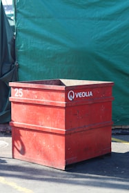Red veolia bin sits in front of green backdrop.