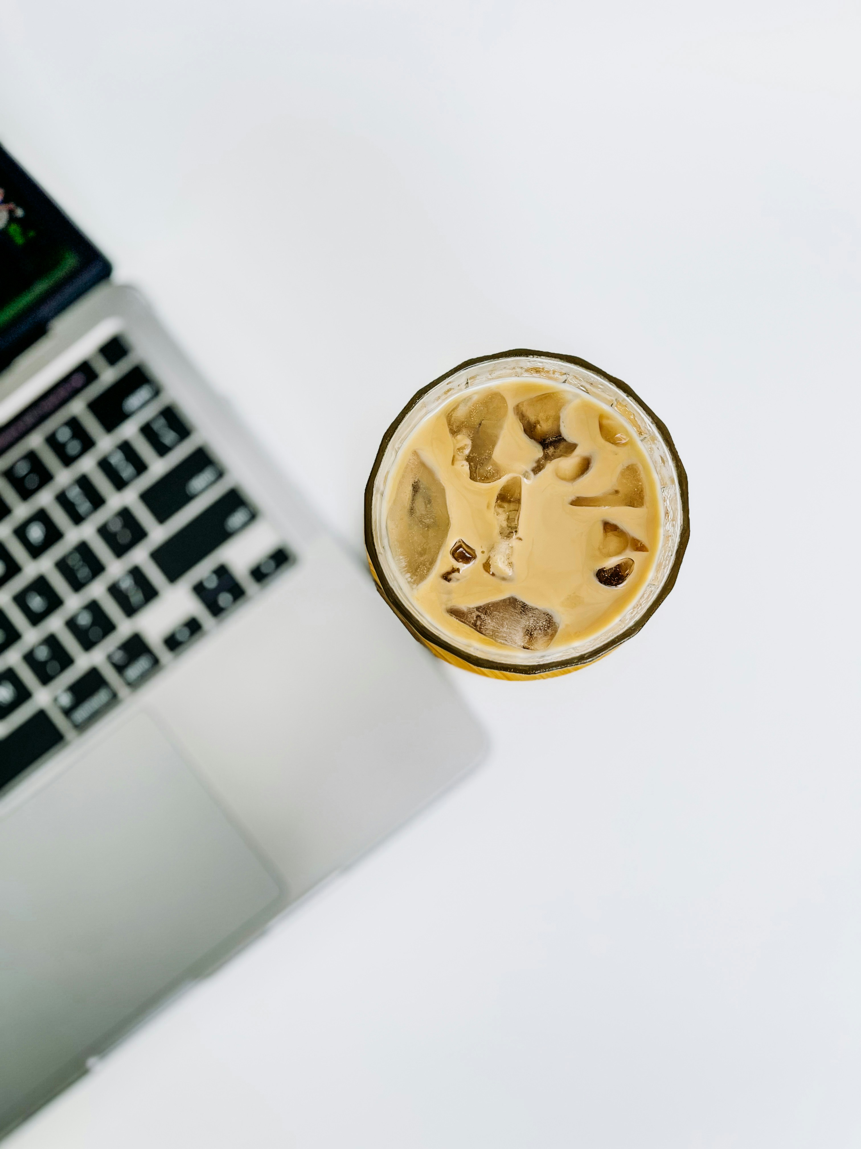 Laptop and iced coffee on a white surface.