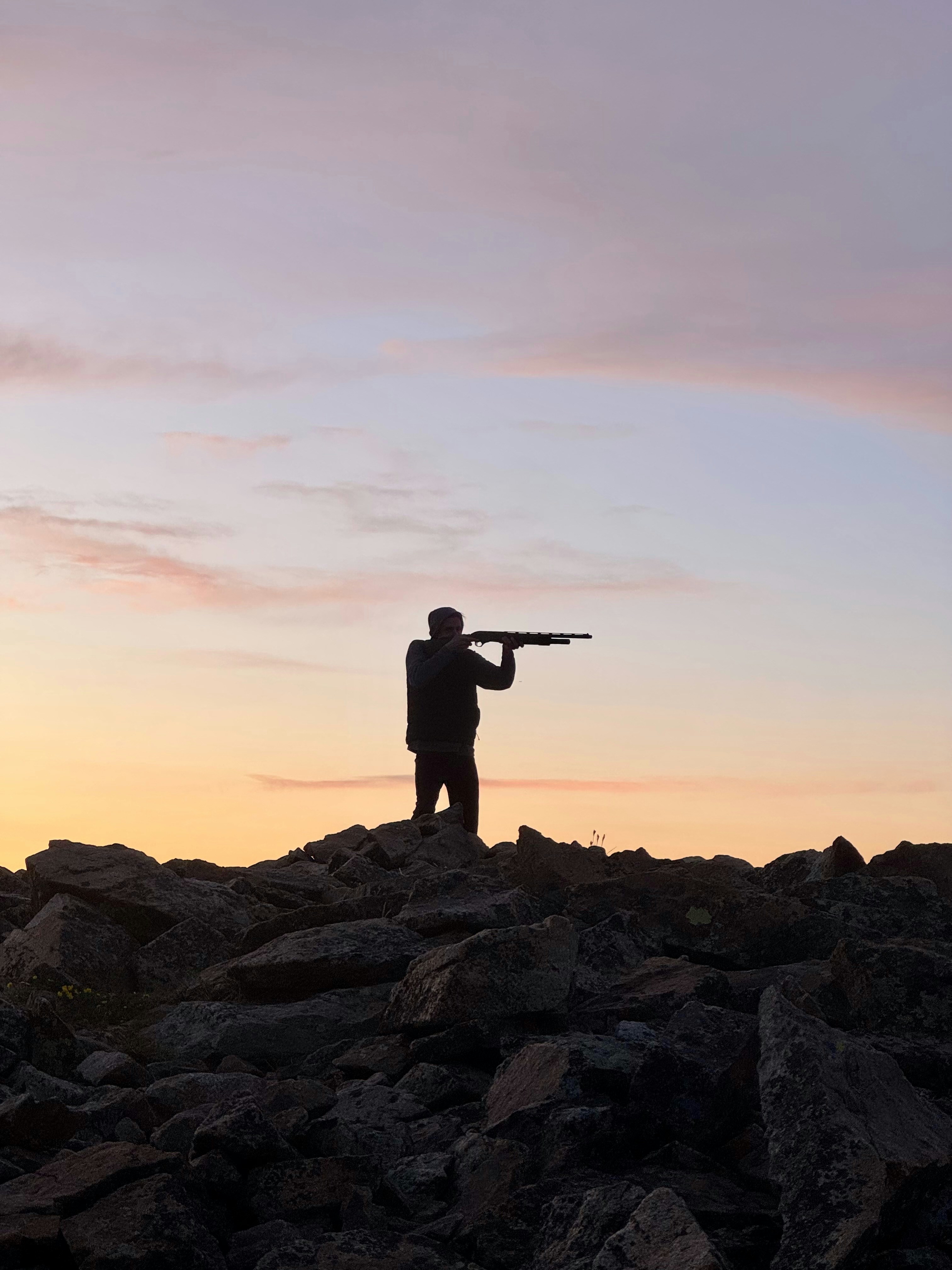 A man aims a rifle against the sunset.