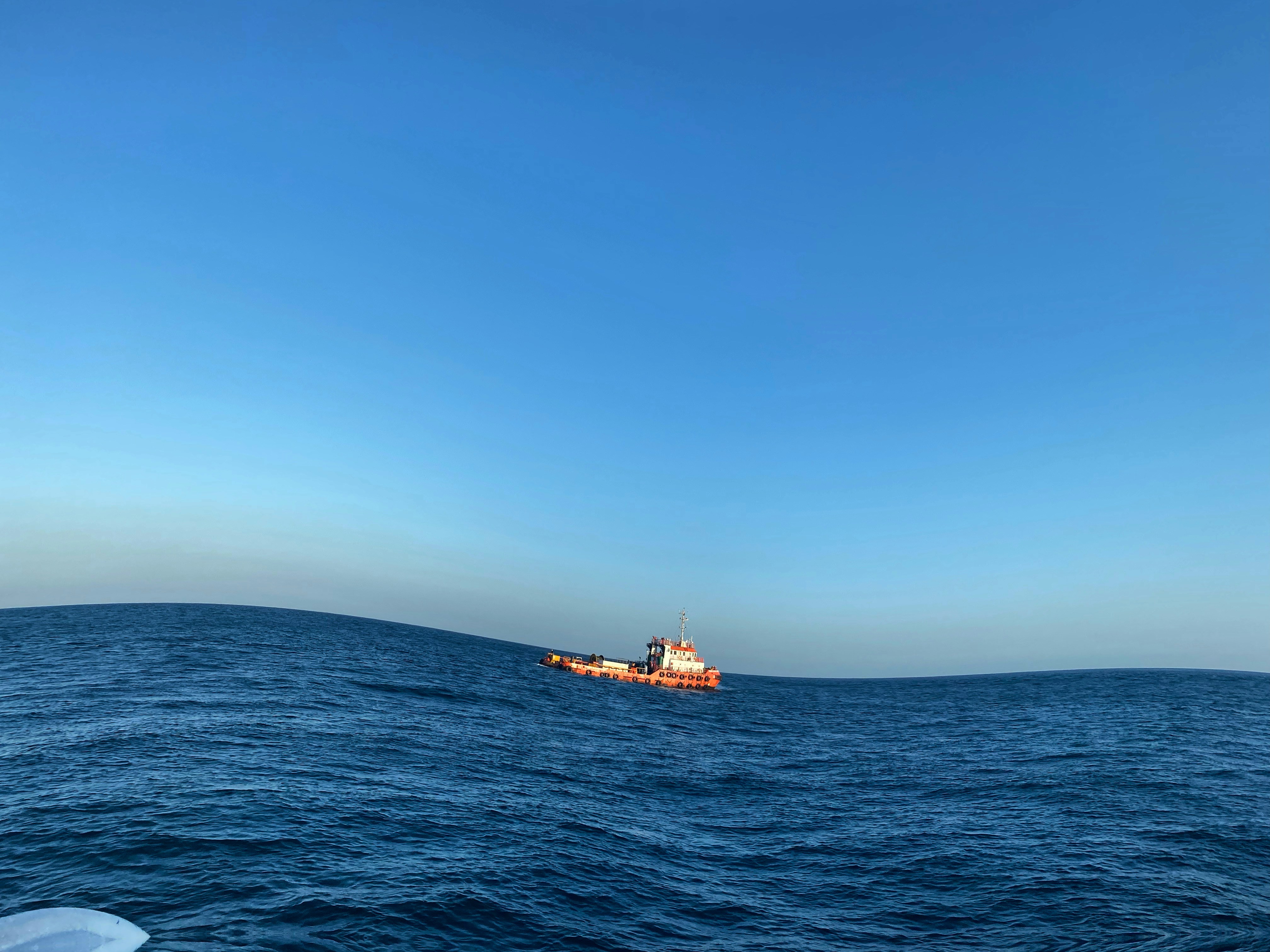 Indian Navy EOD team members in diving gear approaching an oil tanker in the open sea, with a large naval vessel in the background.
