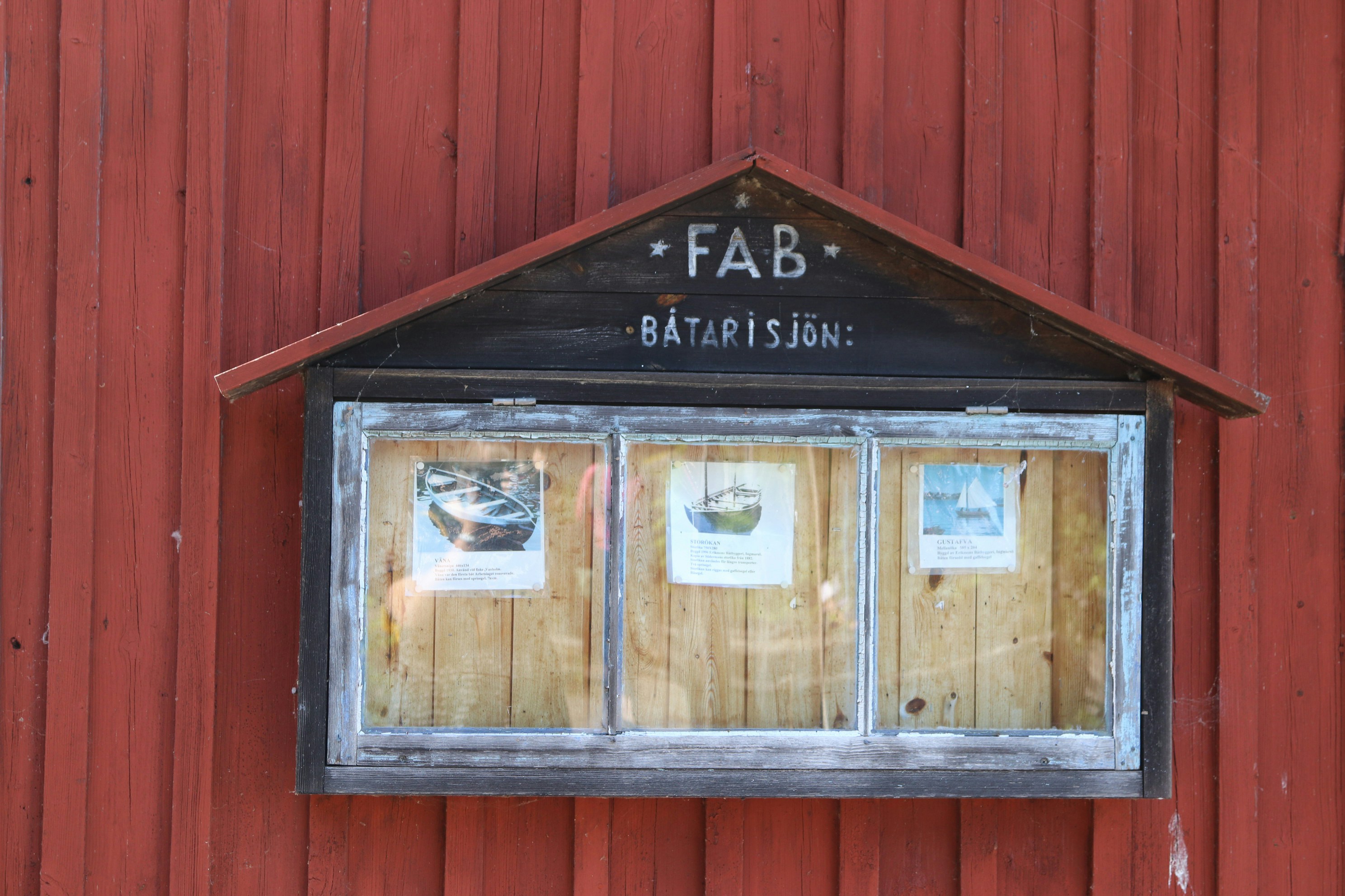A bulletin board hangs on a red building.