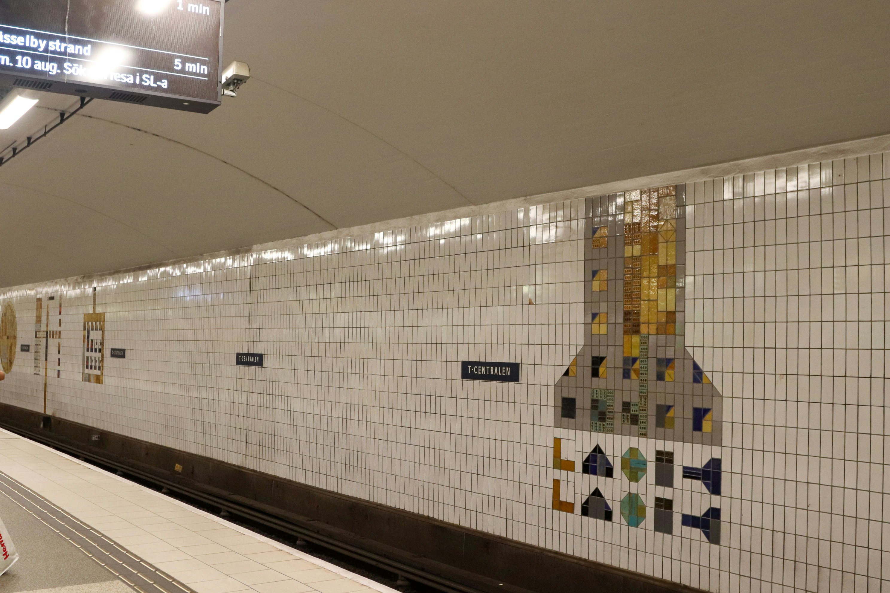 Subway platform with tiled walls and art.