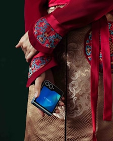 A person holds a foldable phone in ornate clothing.