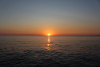 The sun sets over a calm, vast ocean.
