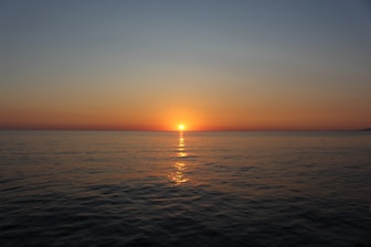 The sun sets over a calm, vast ocean.