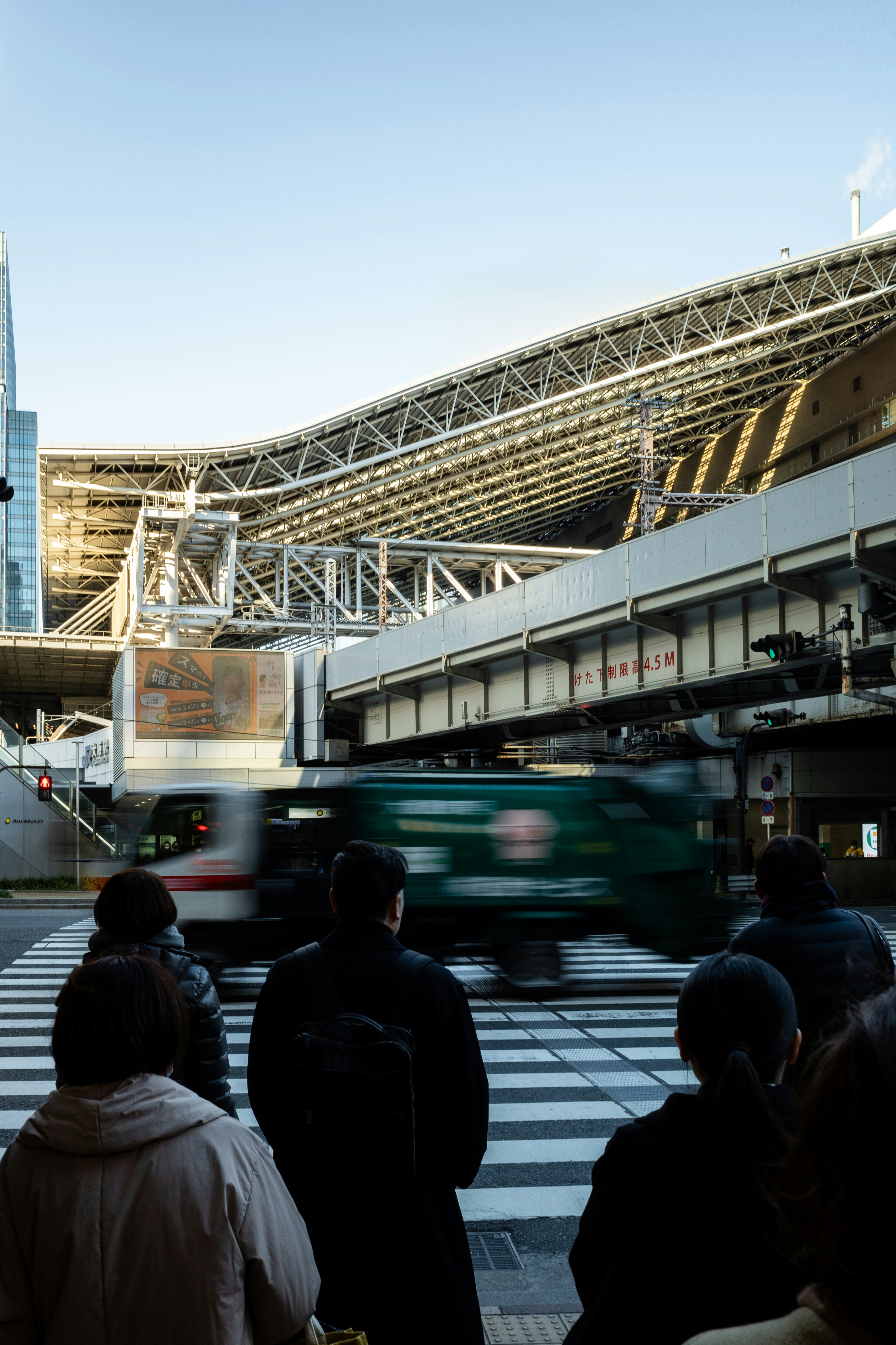 People wait to cross a busy street with a blurred train