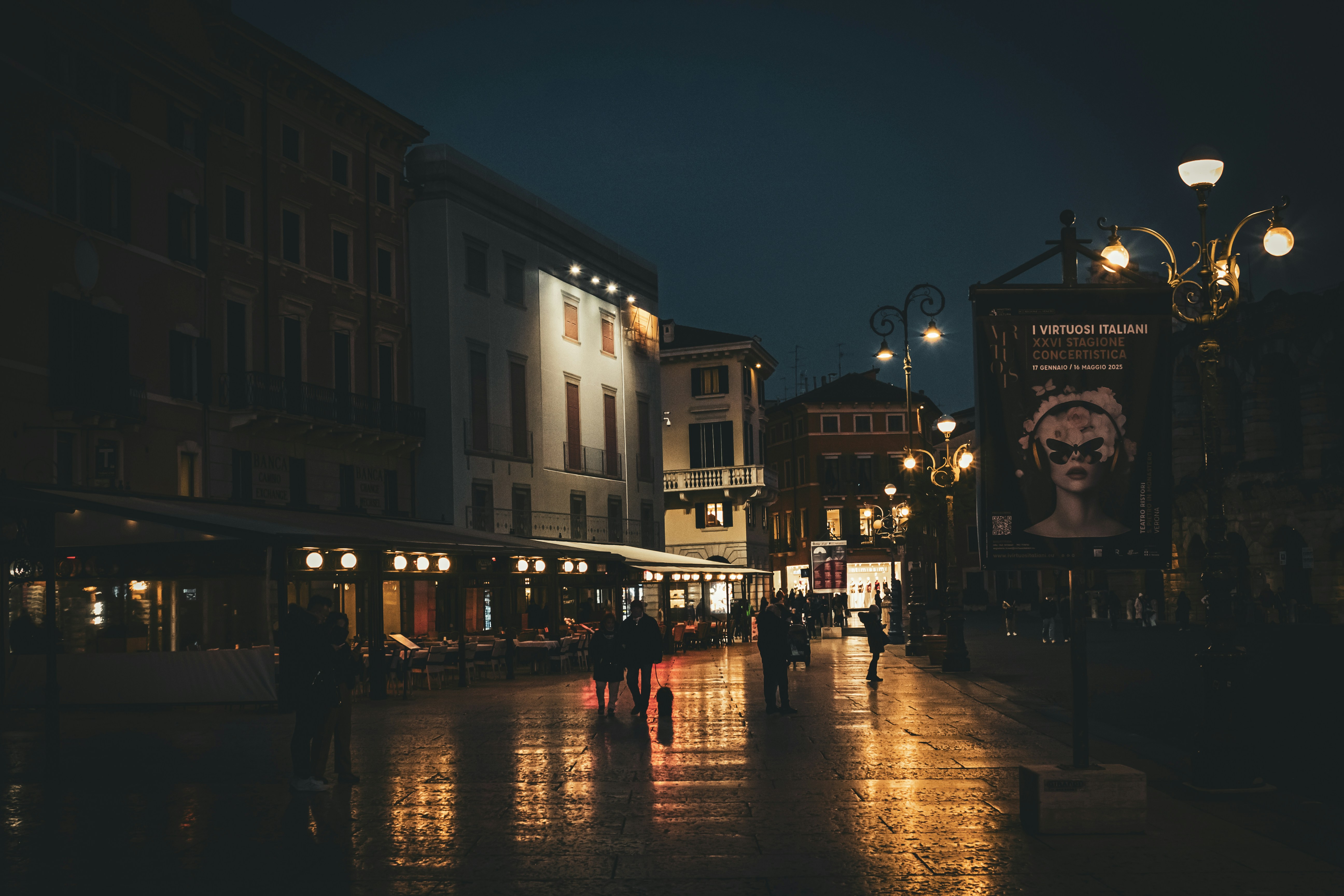 Nighttime city street with lights reflecting in puddles.