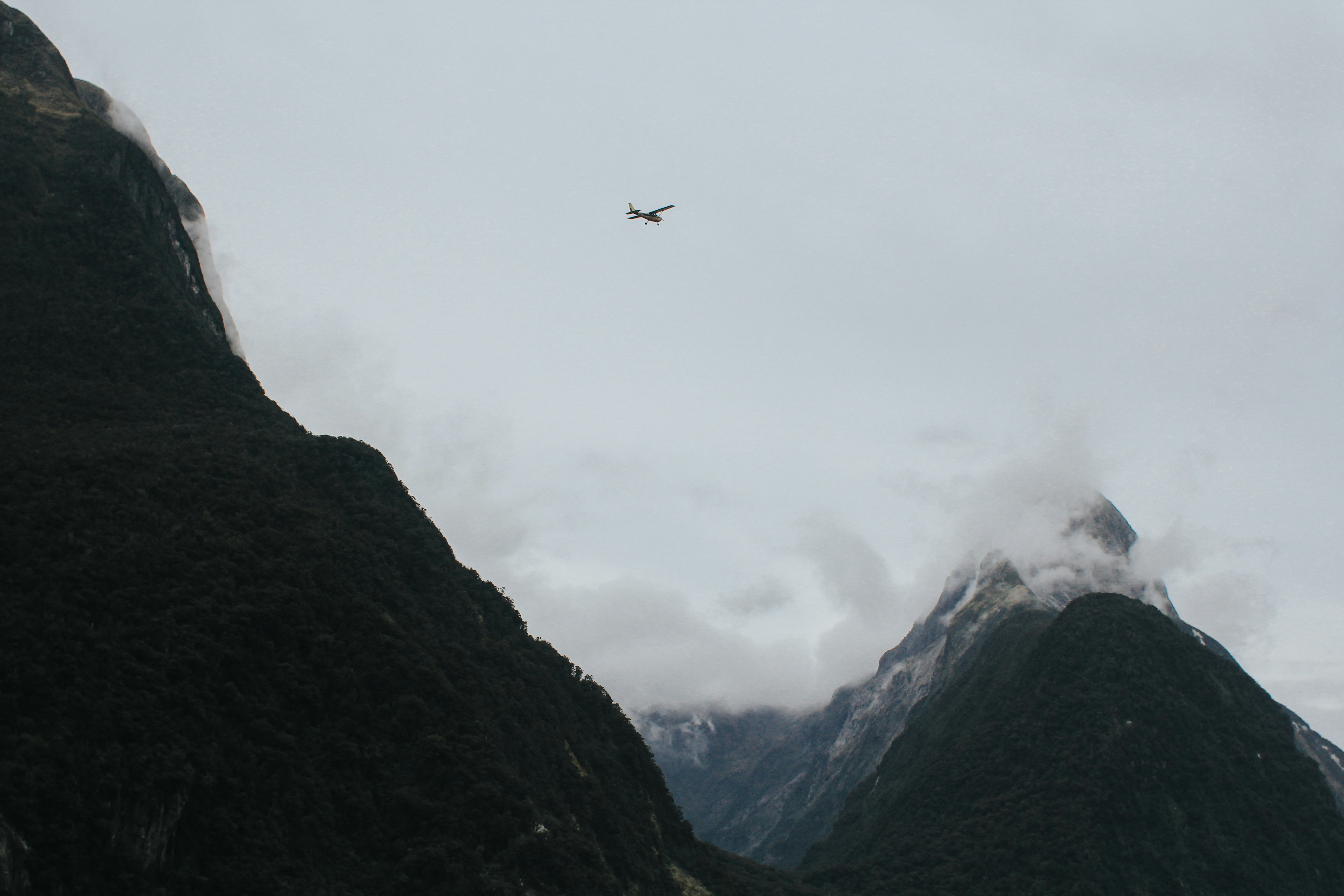 A plane flies over mountains in cloudy skies.