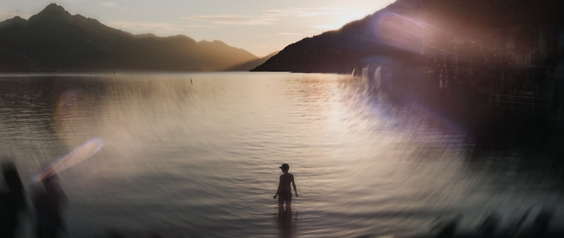 A person stands in the water at sunset.