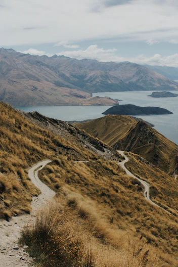 A winding path overlooks a lake and mountains.