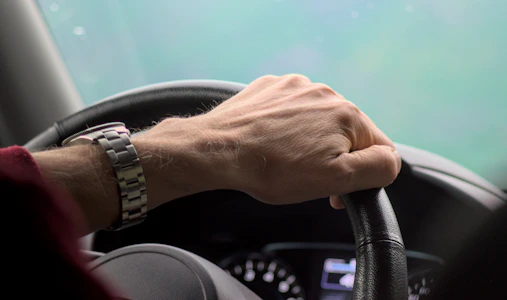 Hand gripping a steering wheel while driving.