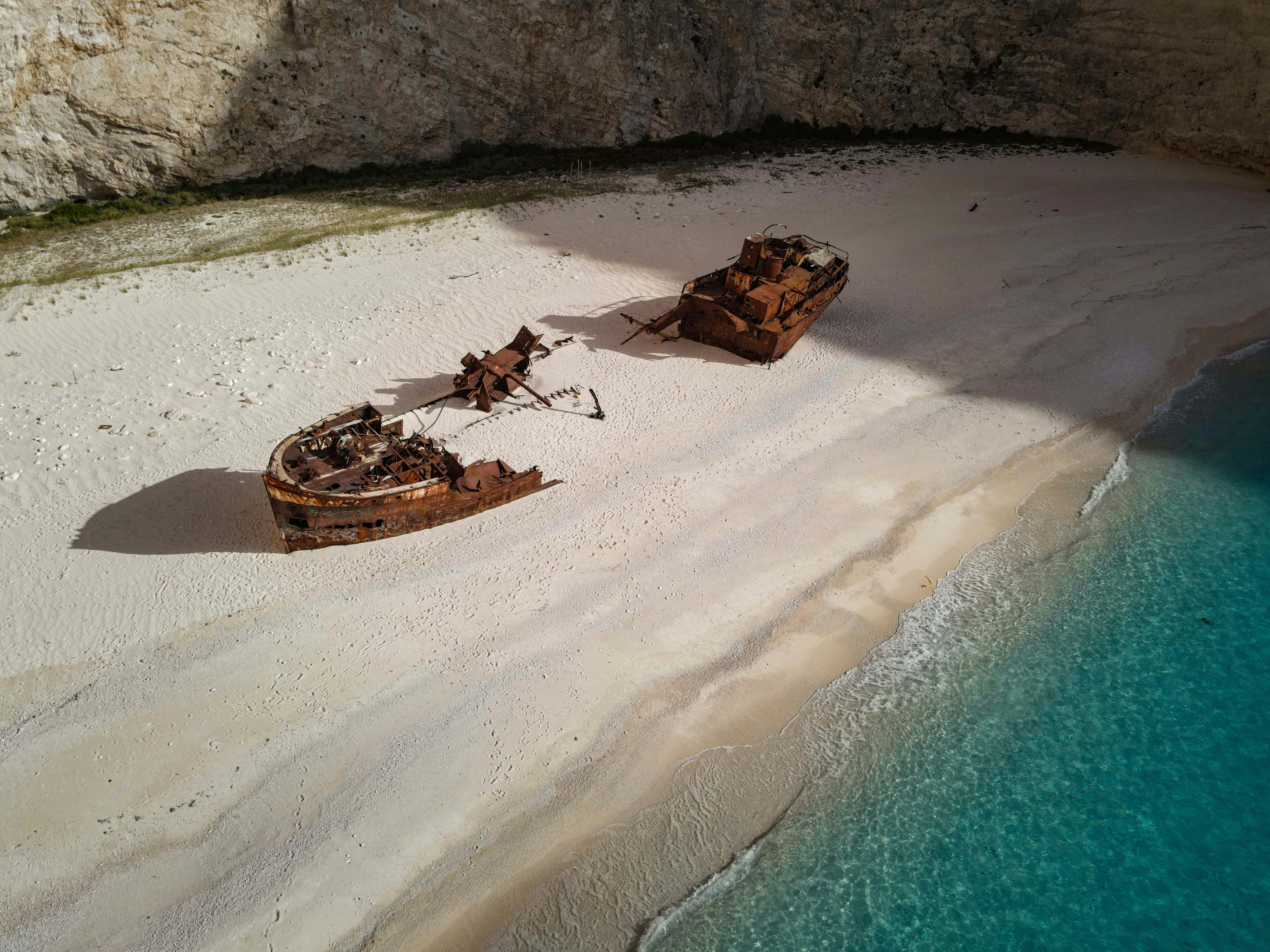 A shipwreck rests on a pristine sandy beach.