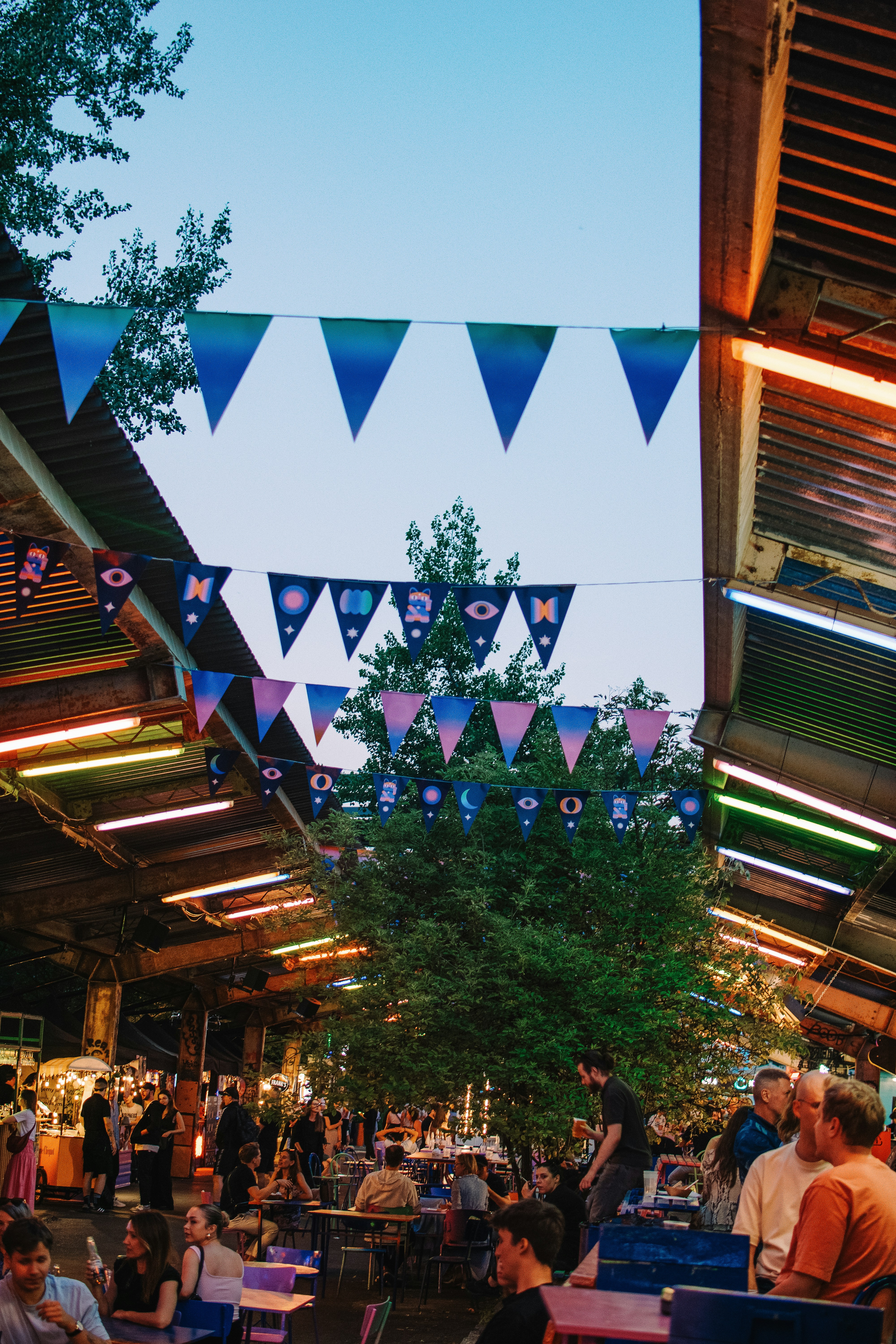 People dine under colorful banners and lights.