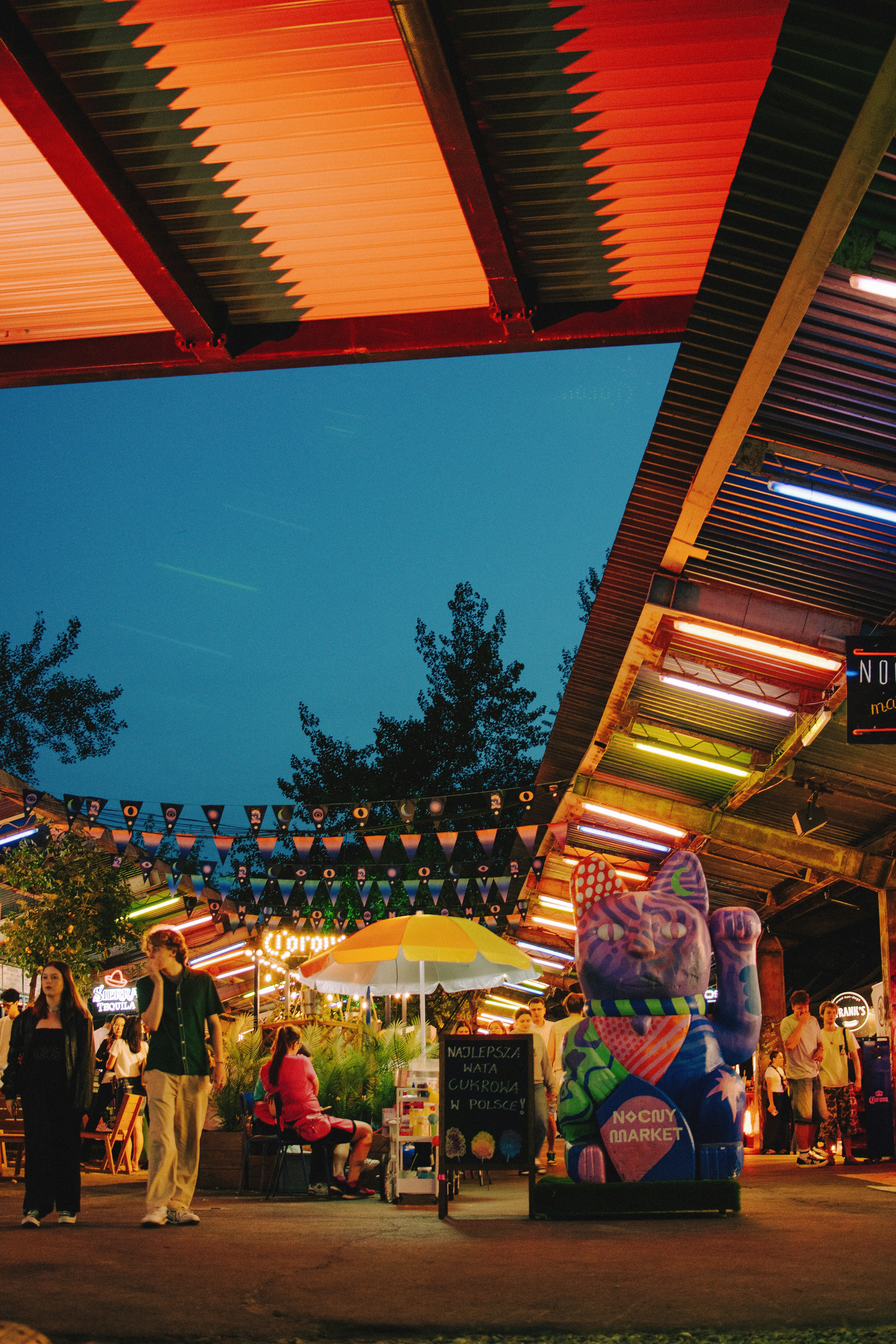 People enjoy a night market under colorful lights.