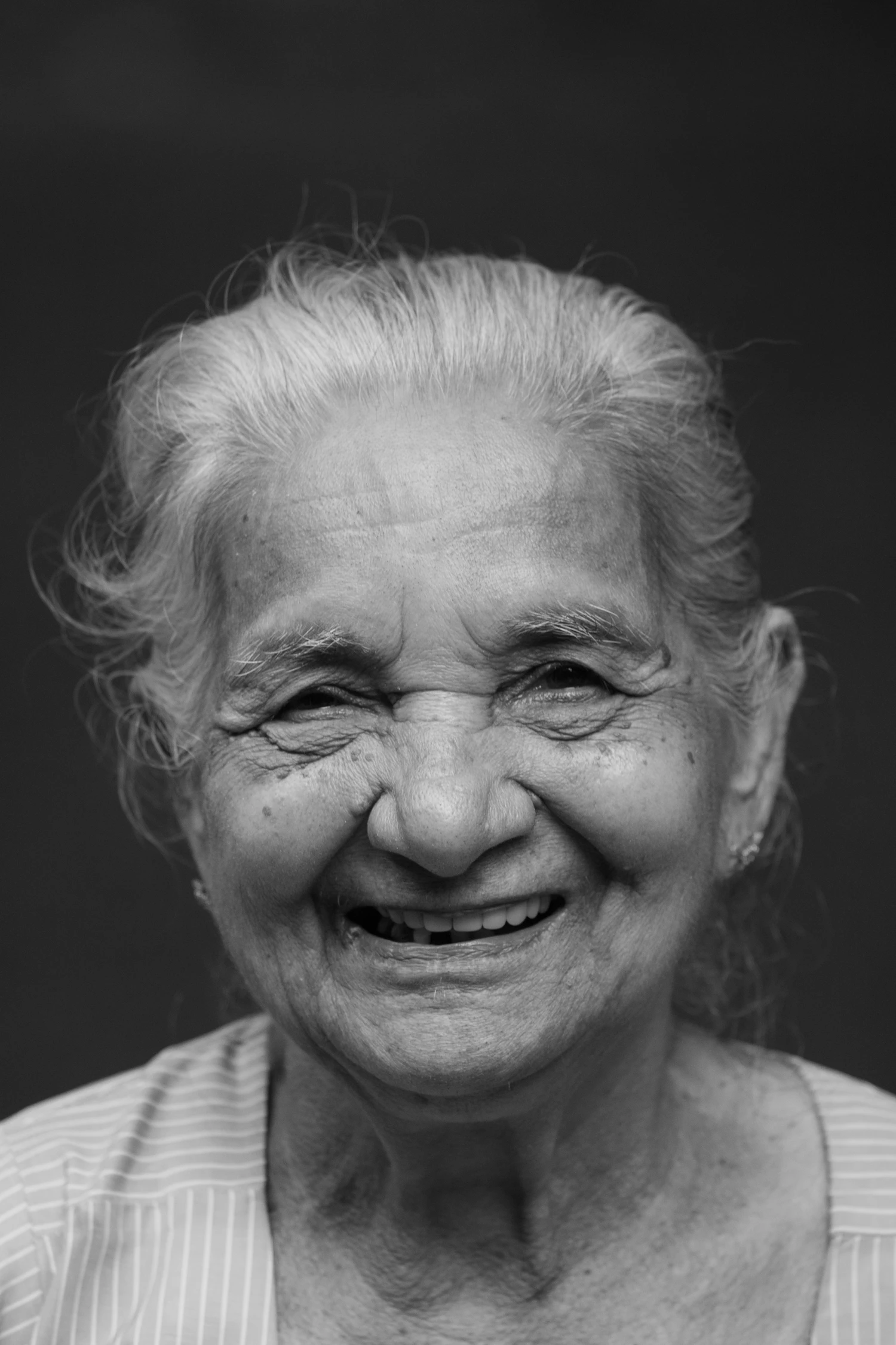 An older woman laughing, photographed against a pale wall