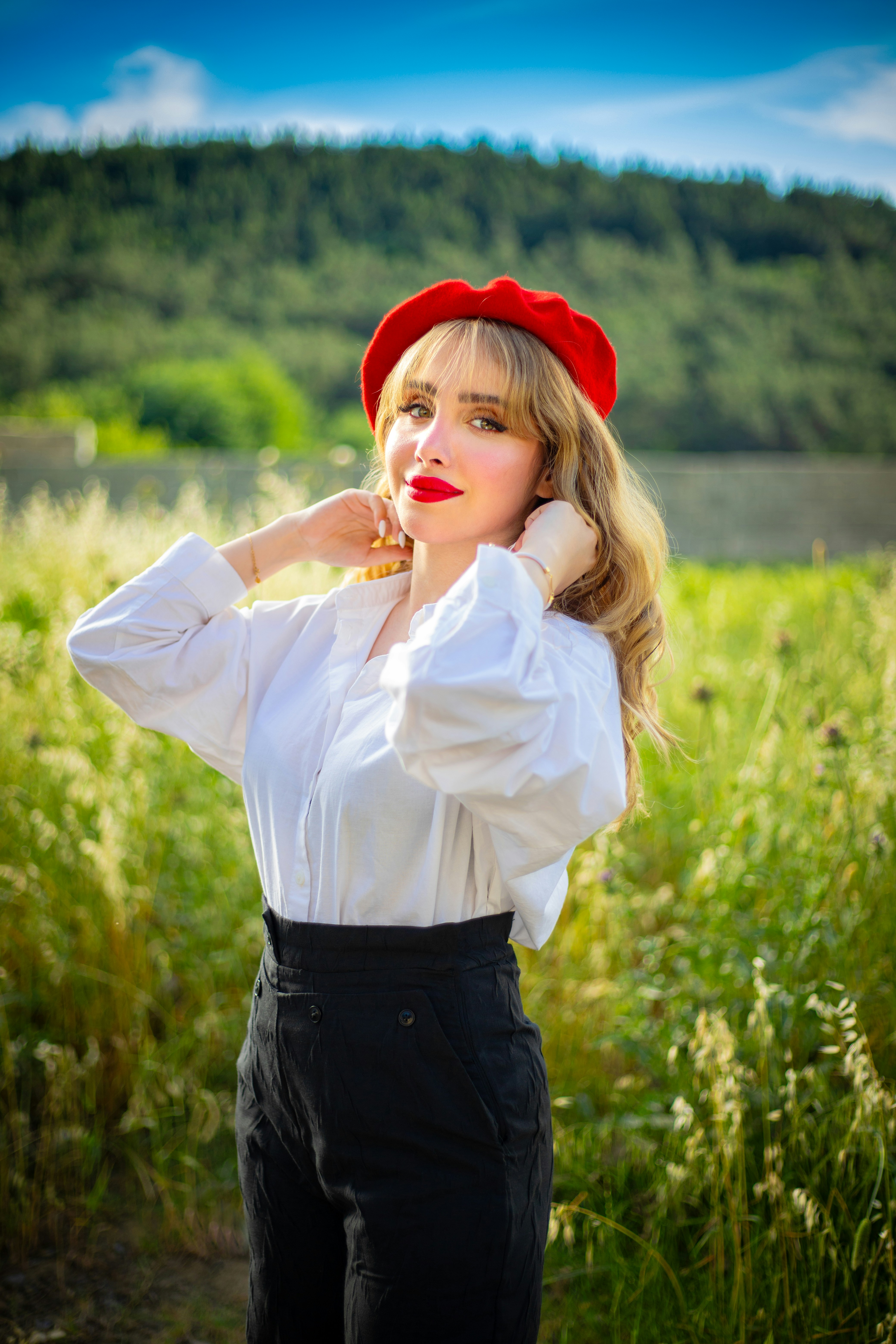 Femme pose gracieusement dans un champ, vêtue d’un béret rouge.