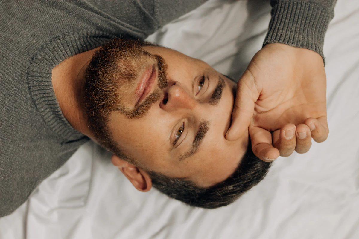 Man lying awake in bed with his hand on his head, unable to sleep, illustrating how poor sleep lowers testosterone.