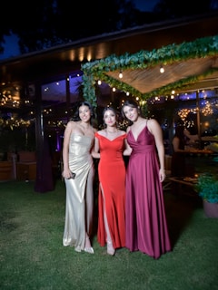 Three women pose together at a fancy outdoor event.