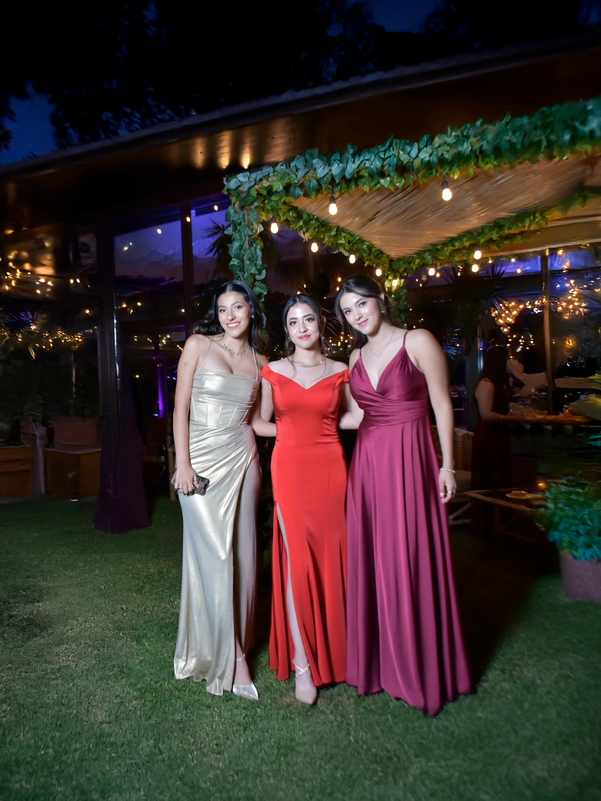 Three women pose together at a fancy outdoor event.