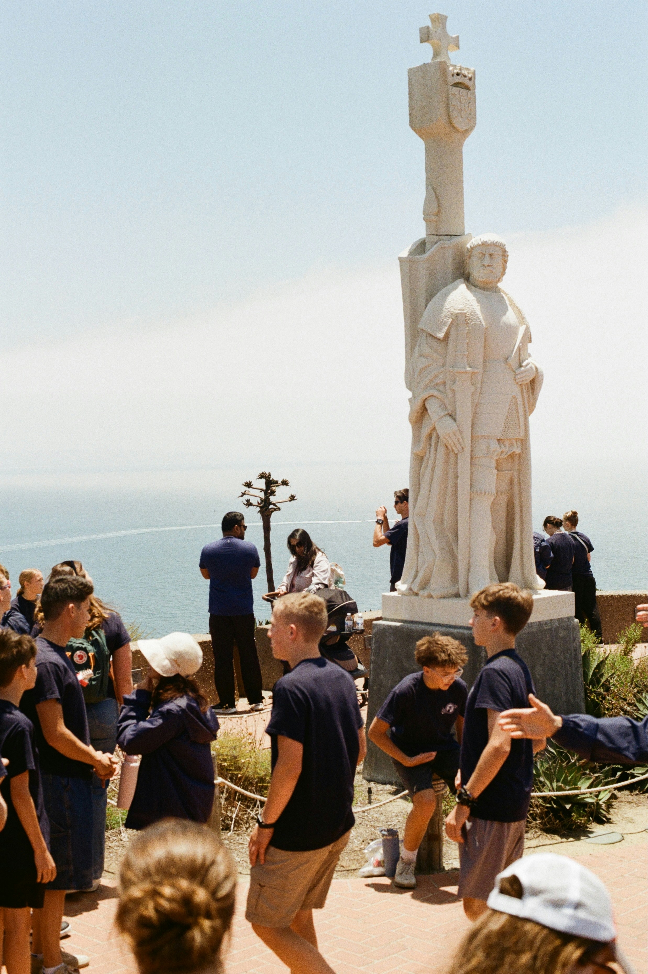 People stand near a statue overlooking the ocean.