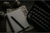 A typewriter, notepad, and crumpled paper are shown.
