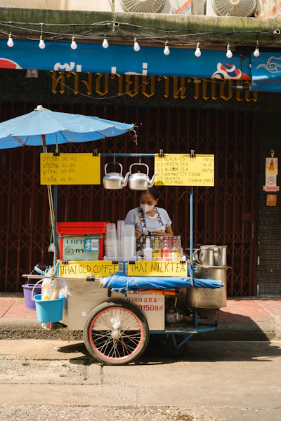 A street vendor serving coffee or tea from a small stand, evoking a local coffee-stop gathering spot