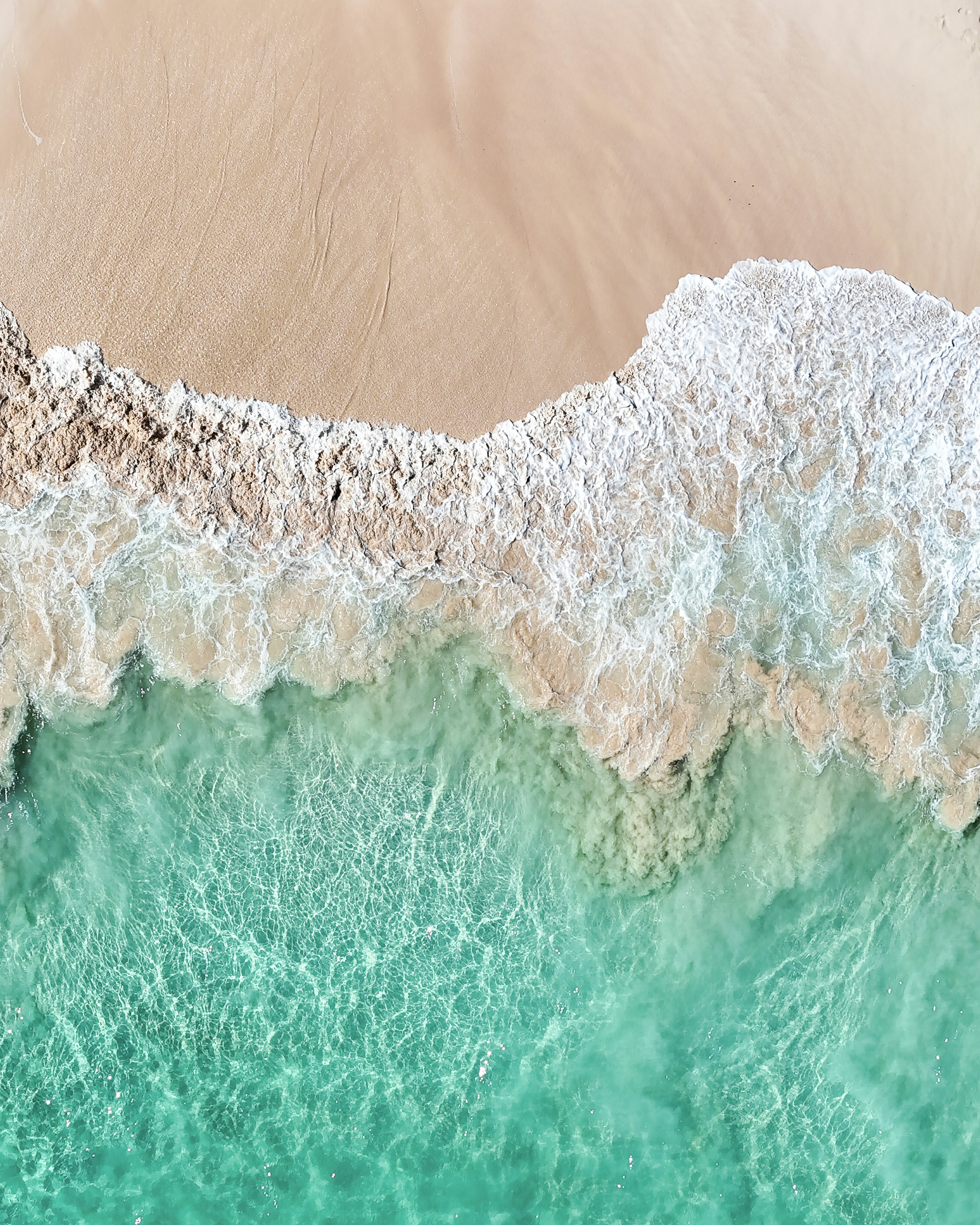 Waves crash on the sandy beach with turquoise water.