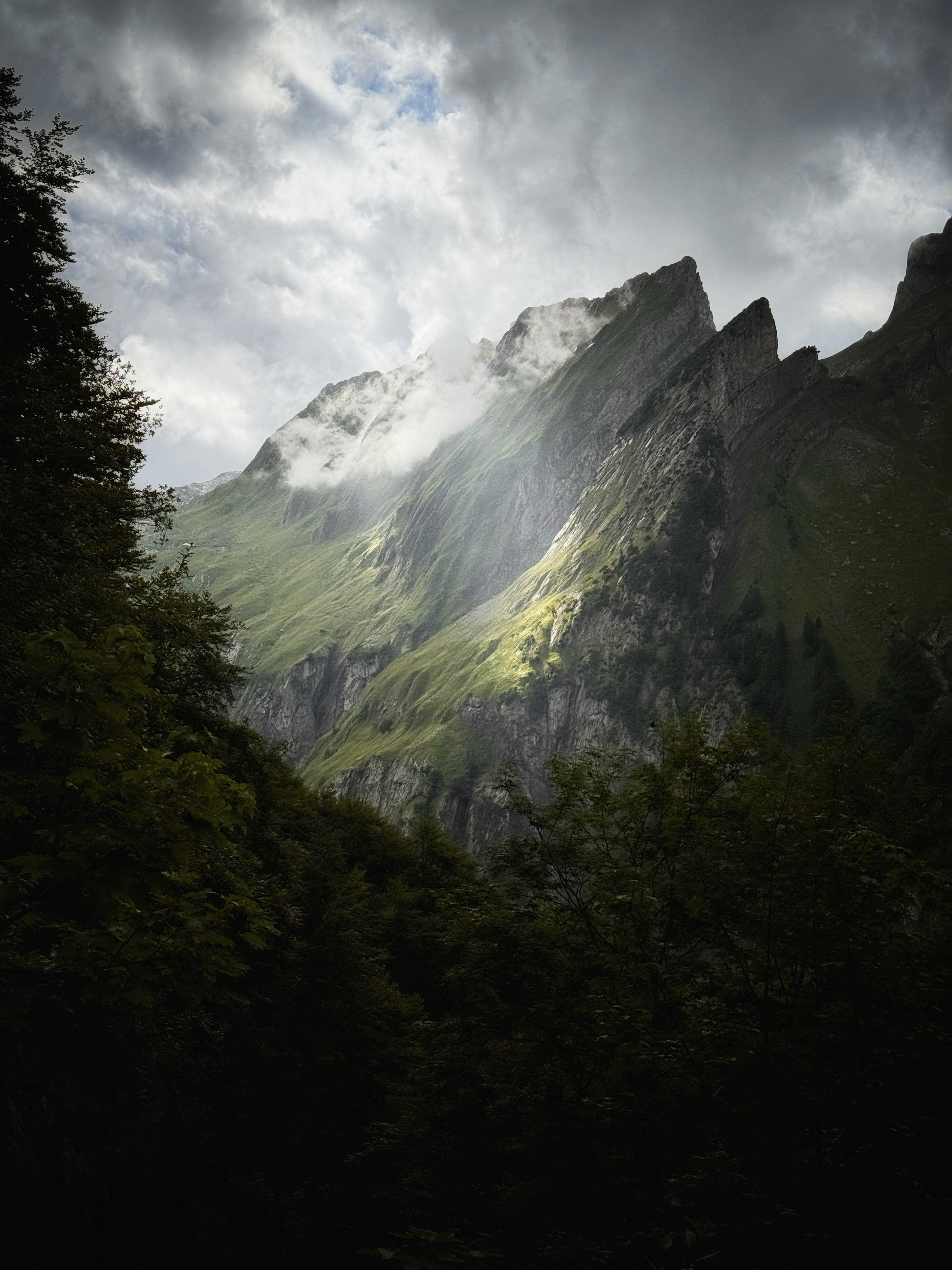 Mountains are revealed by sunlight through dramatic clouds.