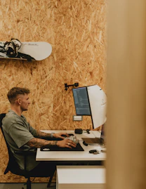A man works at his computer in a wood-paneled room.
