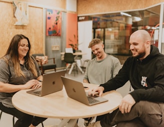 Three people collaborate around a table with laptops.