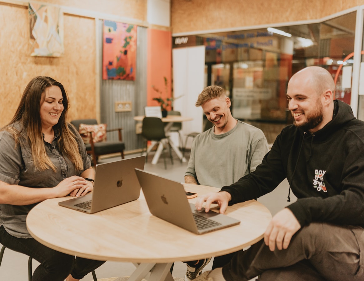Three remote workers on laptops around a wooden table in a coliving common room