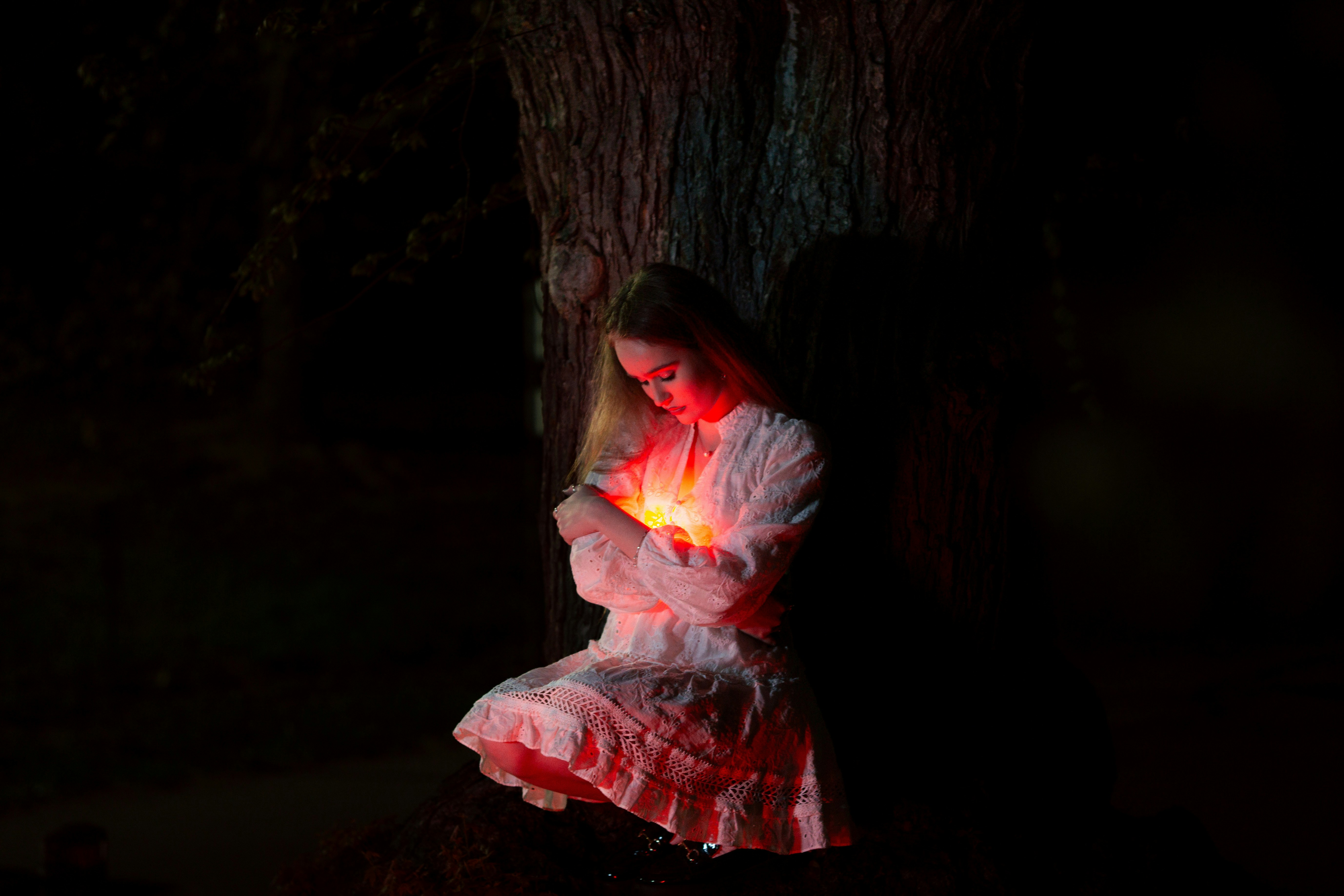 A woman cradles a glowing light in darkness.