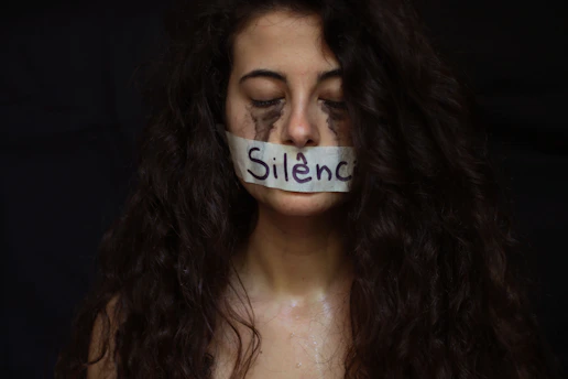 Silence symbolized by tape on a woman's mouth.