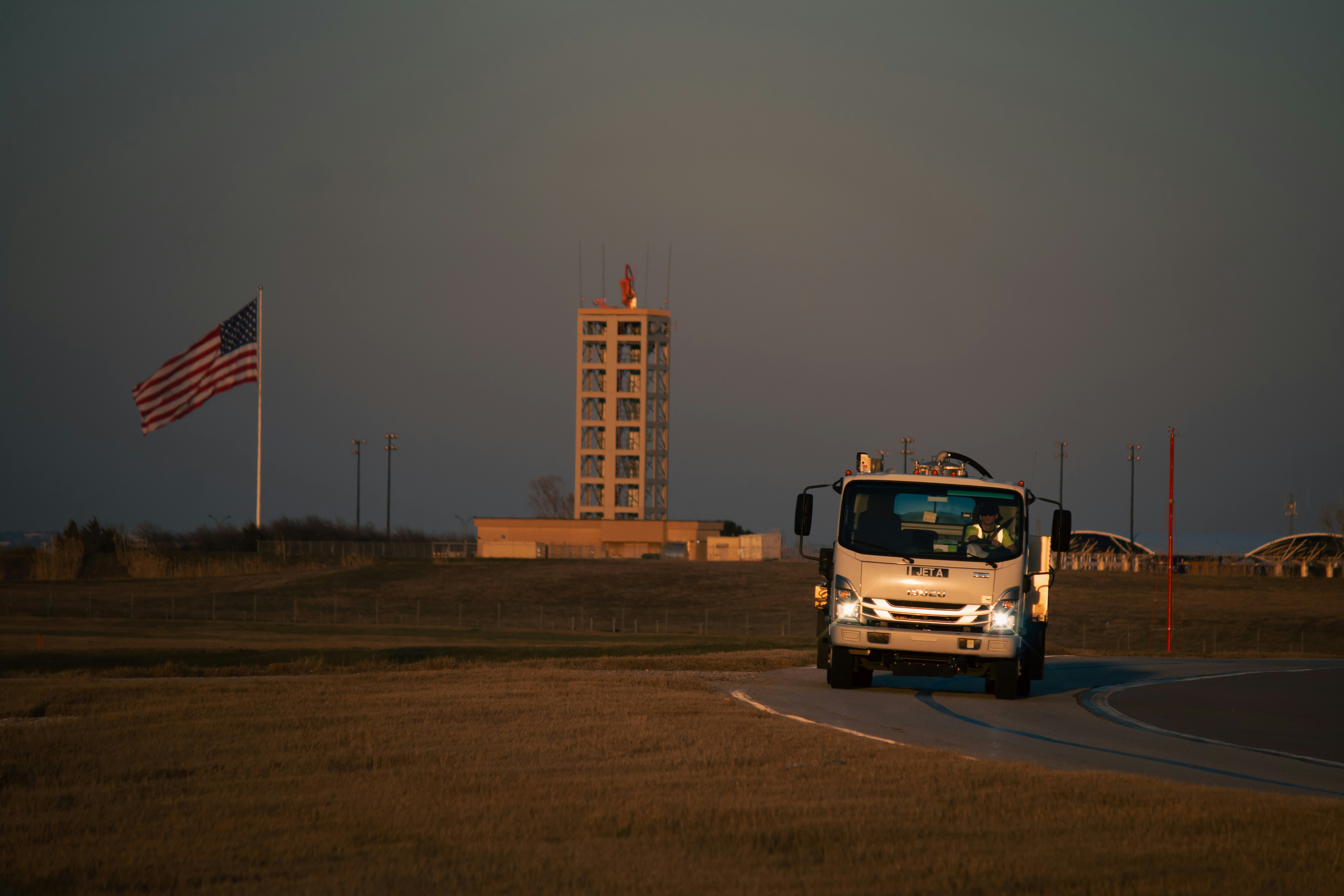 A truck drives past a tower and the american flag.