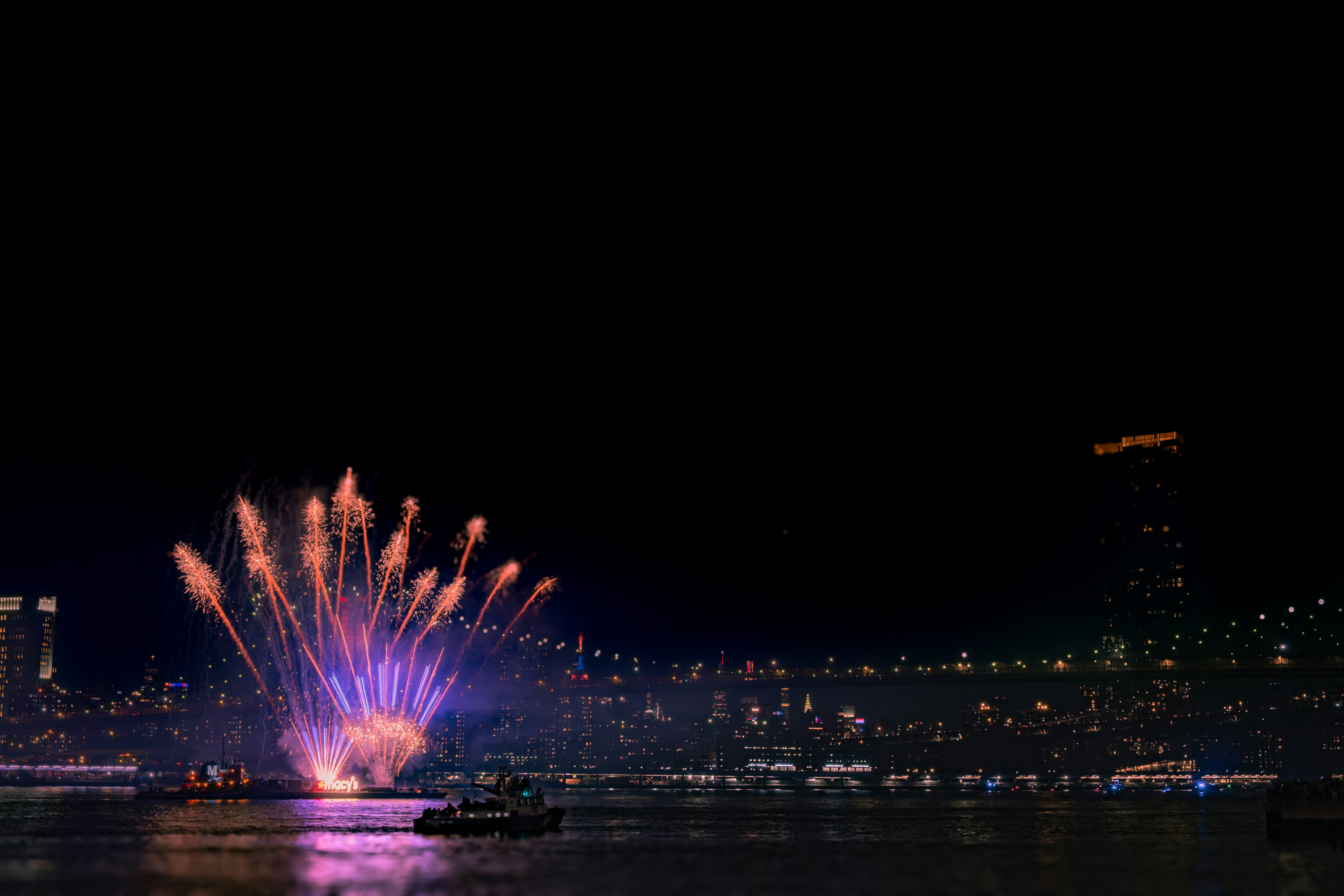 Fireworks illuminate the night sky over the water.