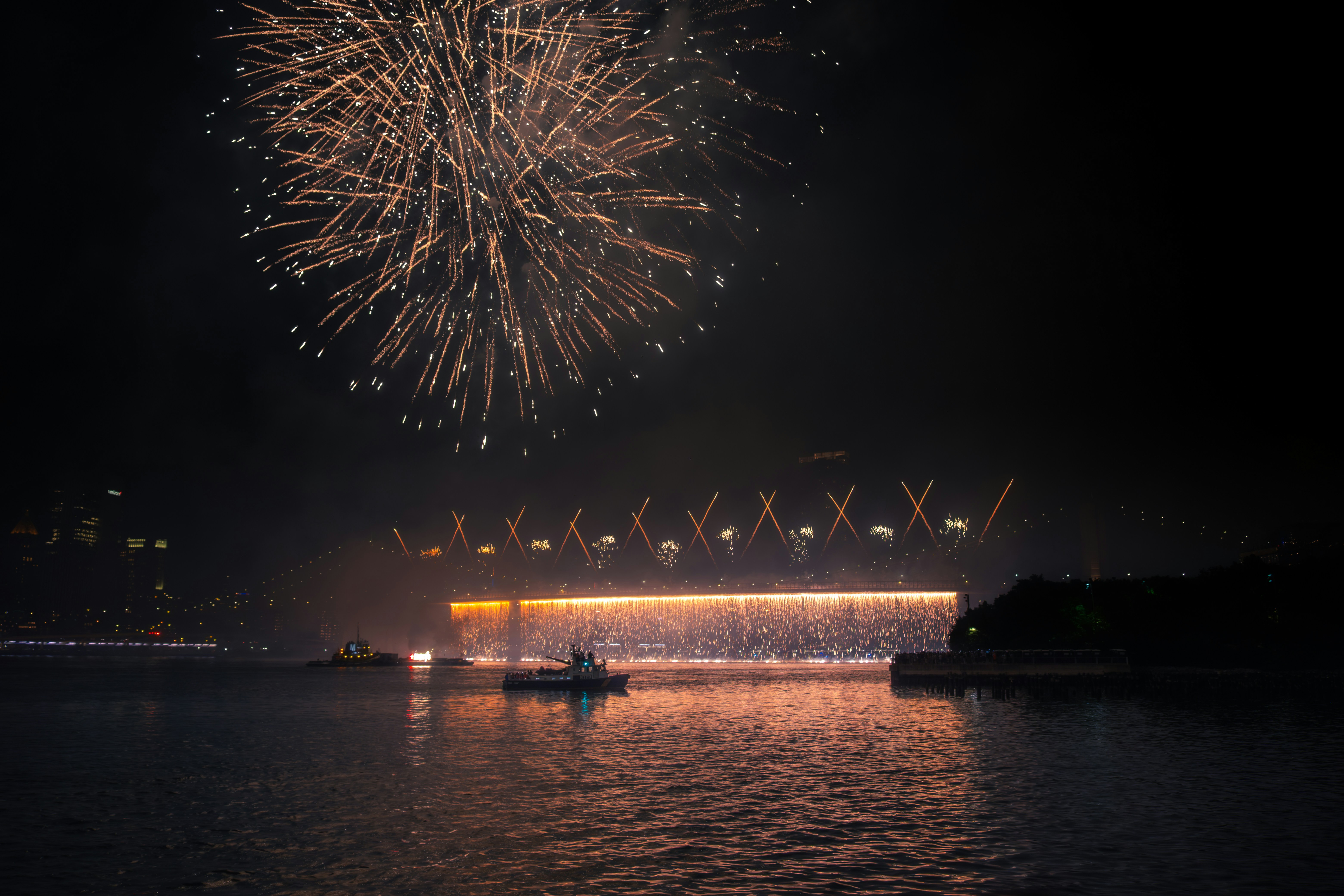 Fireworks explode over a bridge at night.