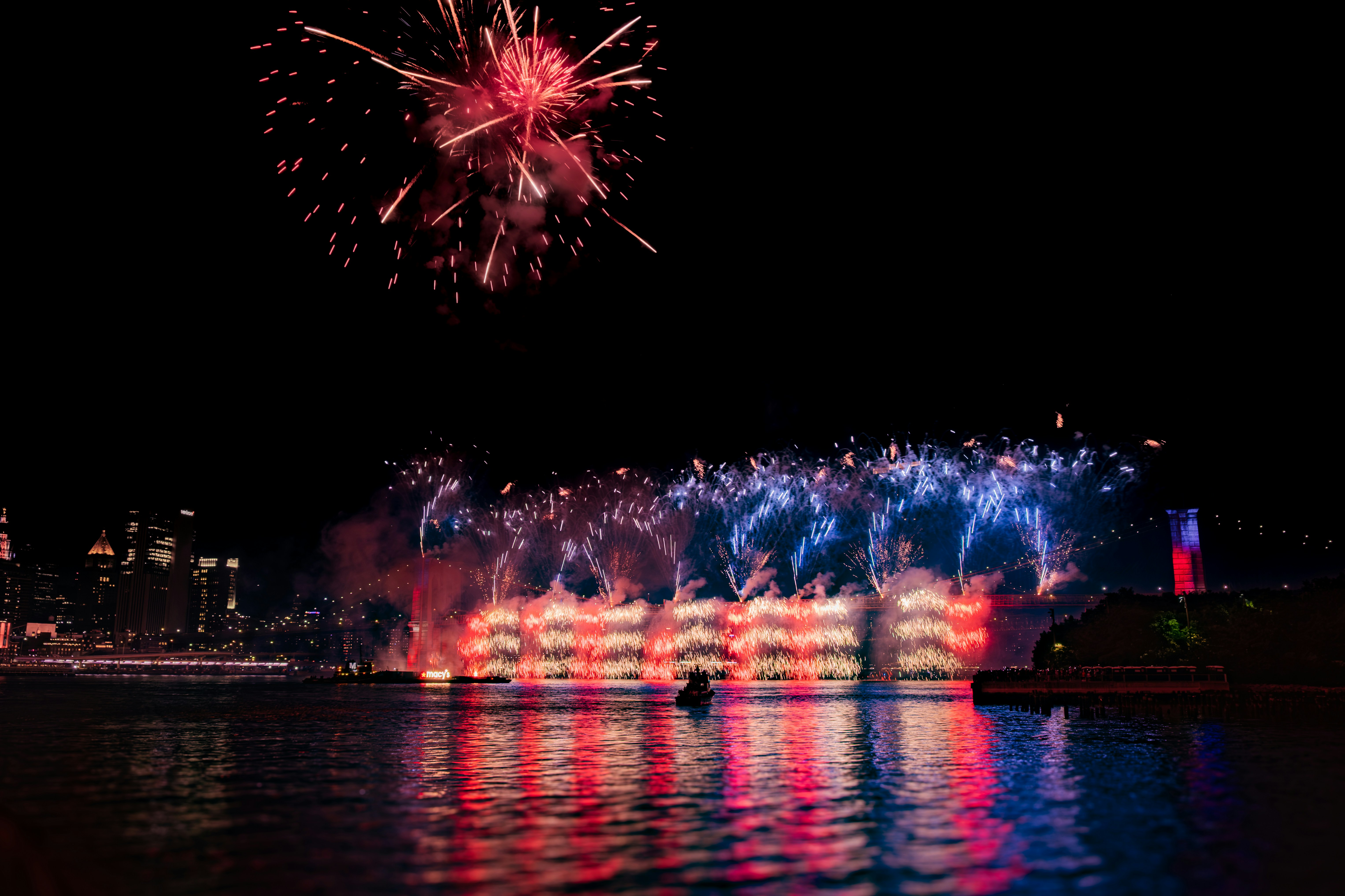 Fireworks illuminate the night sky over water.