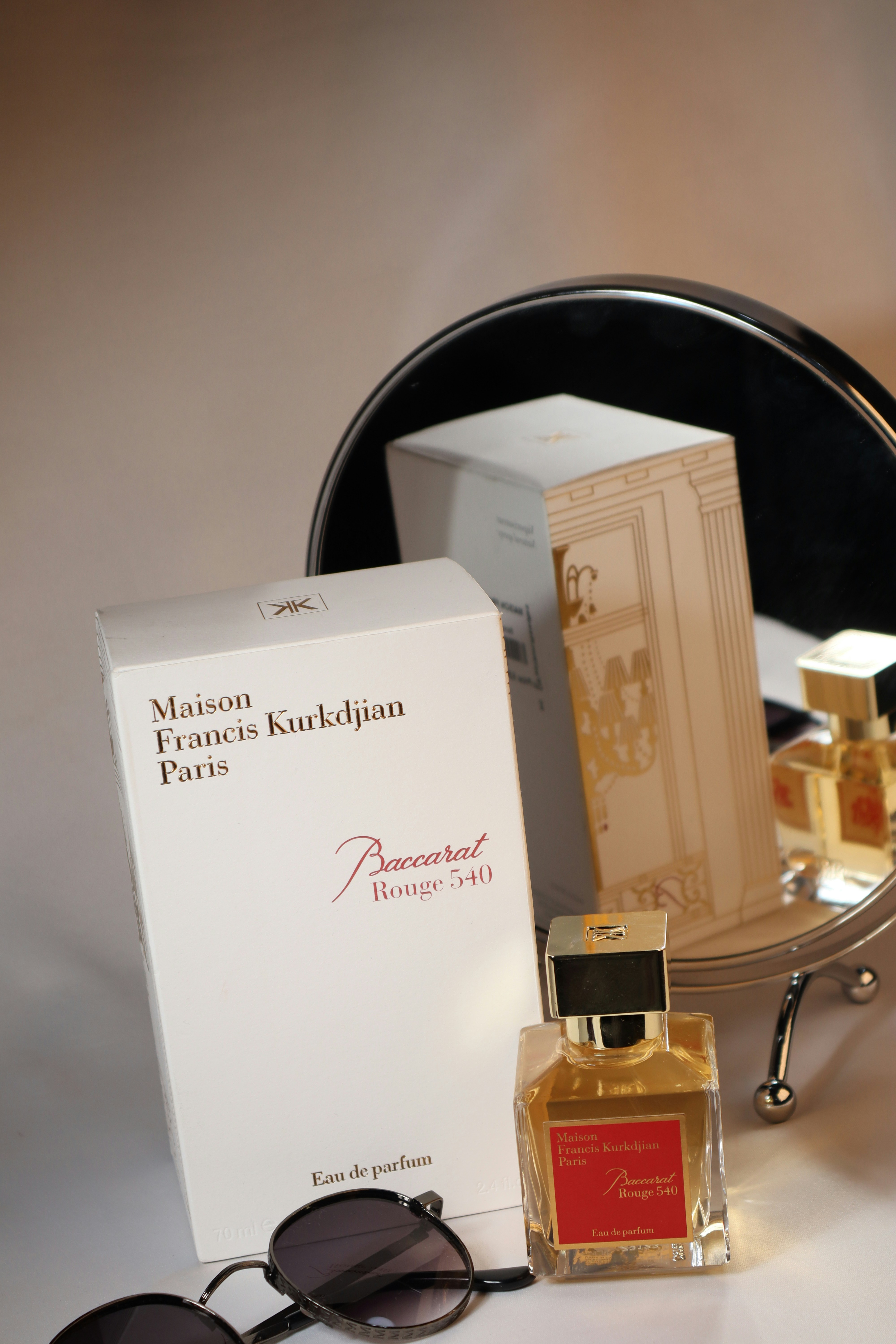 Perfume bottle and boxes with sunglasses sit on a table.