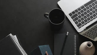 Laptop, mug, and notebooks on a dark workspace