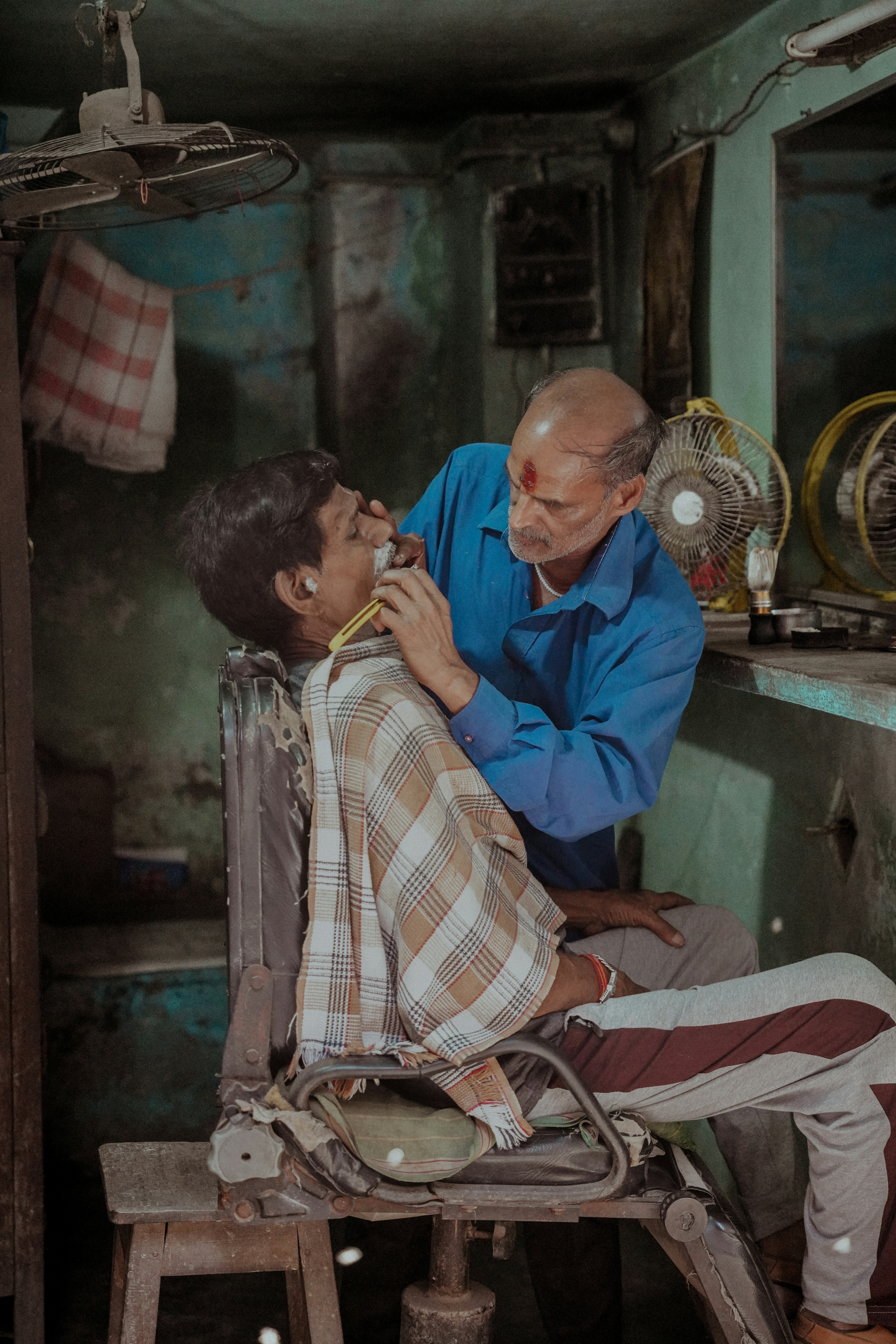 A barber shaves a customer in a rustic shop.