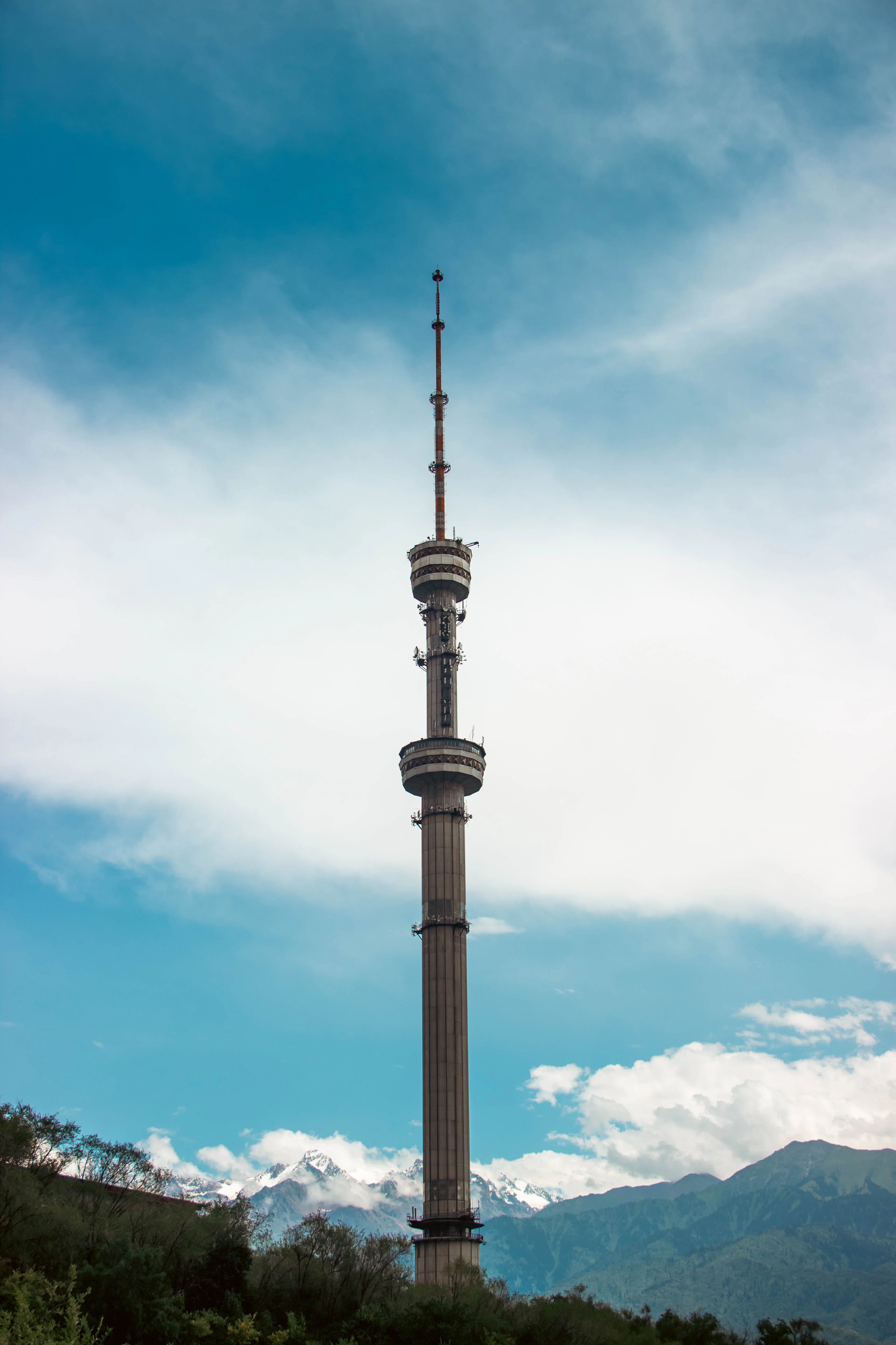 The Kok-Tobe TV tower stands against a blue sky with snow-capped mountains behind it.