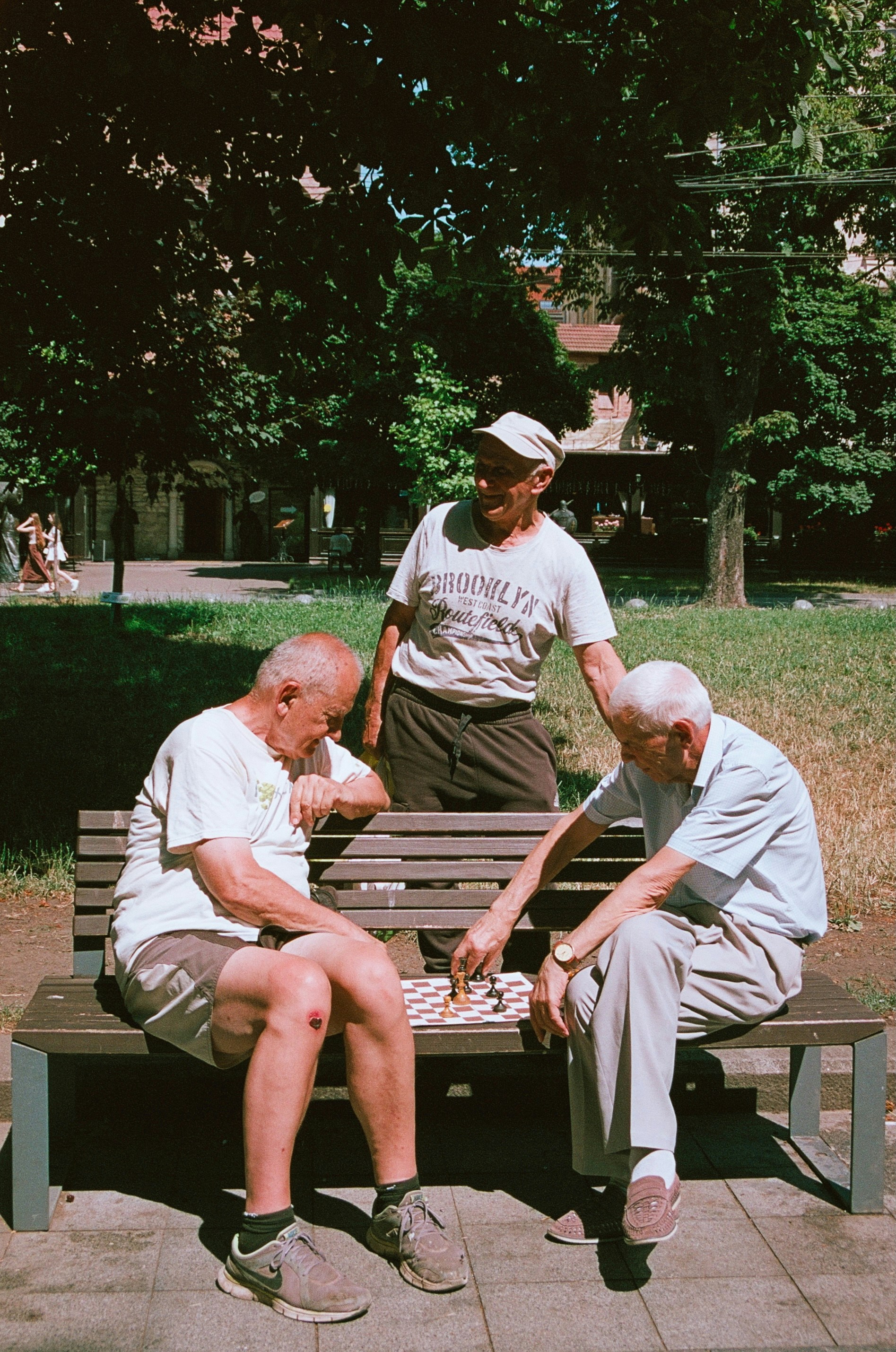 Three older men play checkers on a park bench.