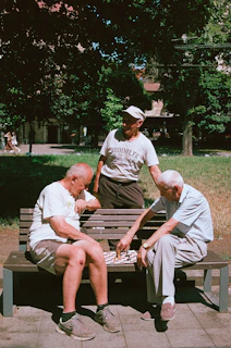 Three older men play checkers on a park bench